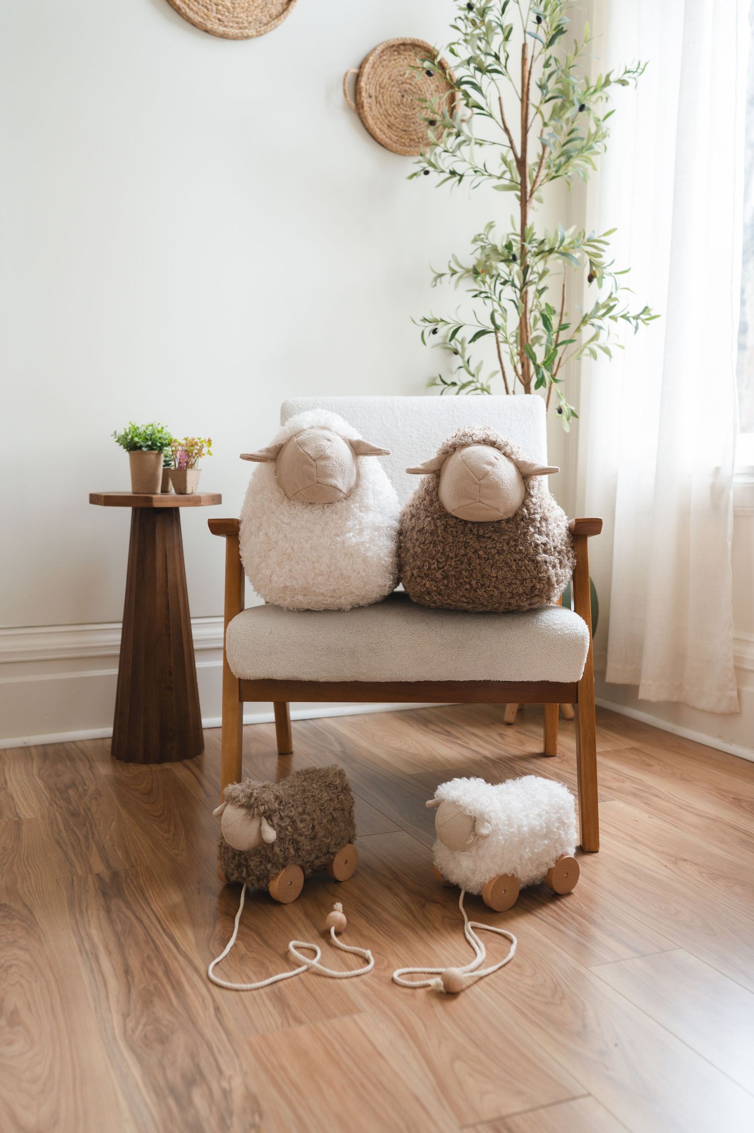 Two fluffy sheep pillows and pull-along lamb toys styled on a wooden armchair.