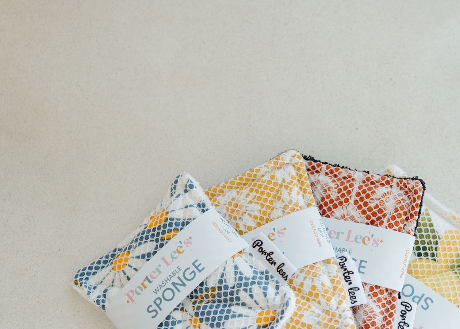 Colorful patterned reusable sponges with floral and geometric designs on a neutral background.