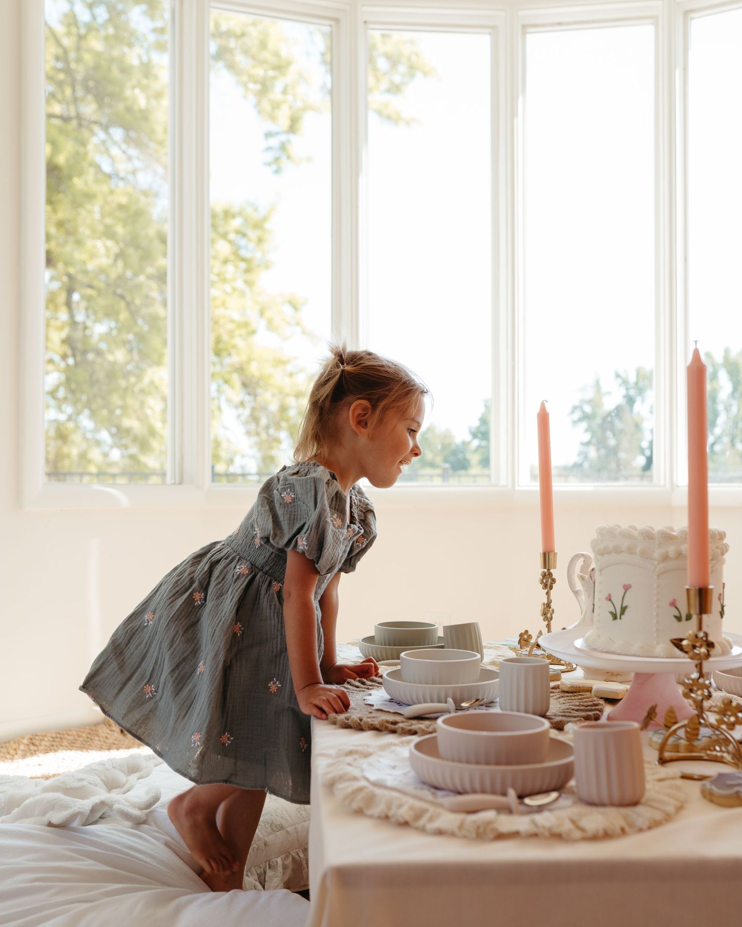 Young girl in floral dress admires a beautifully set birthday party table with cake.