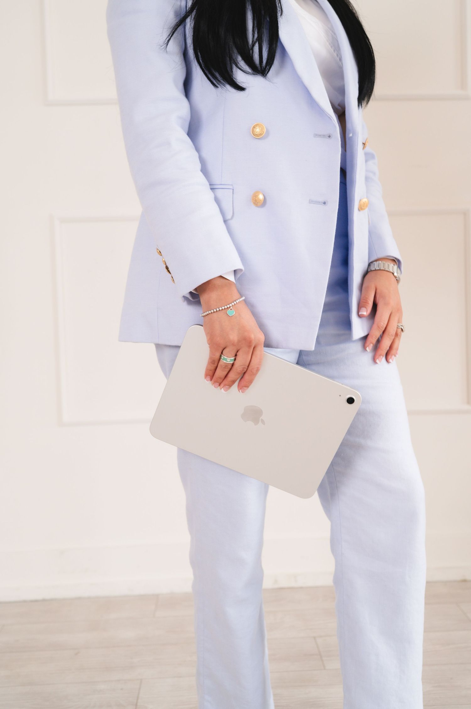 Woman in light blue blazer and pants holding an Apple iPad against white wall.