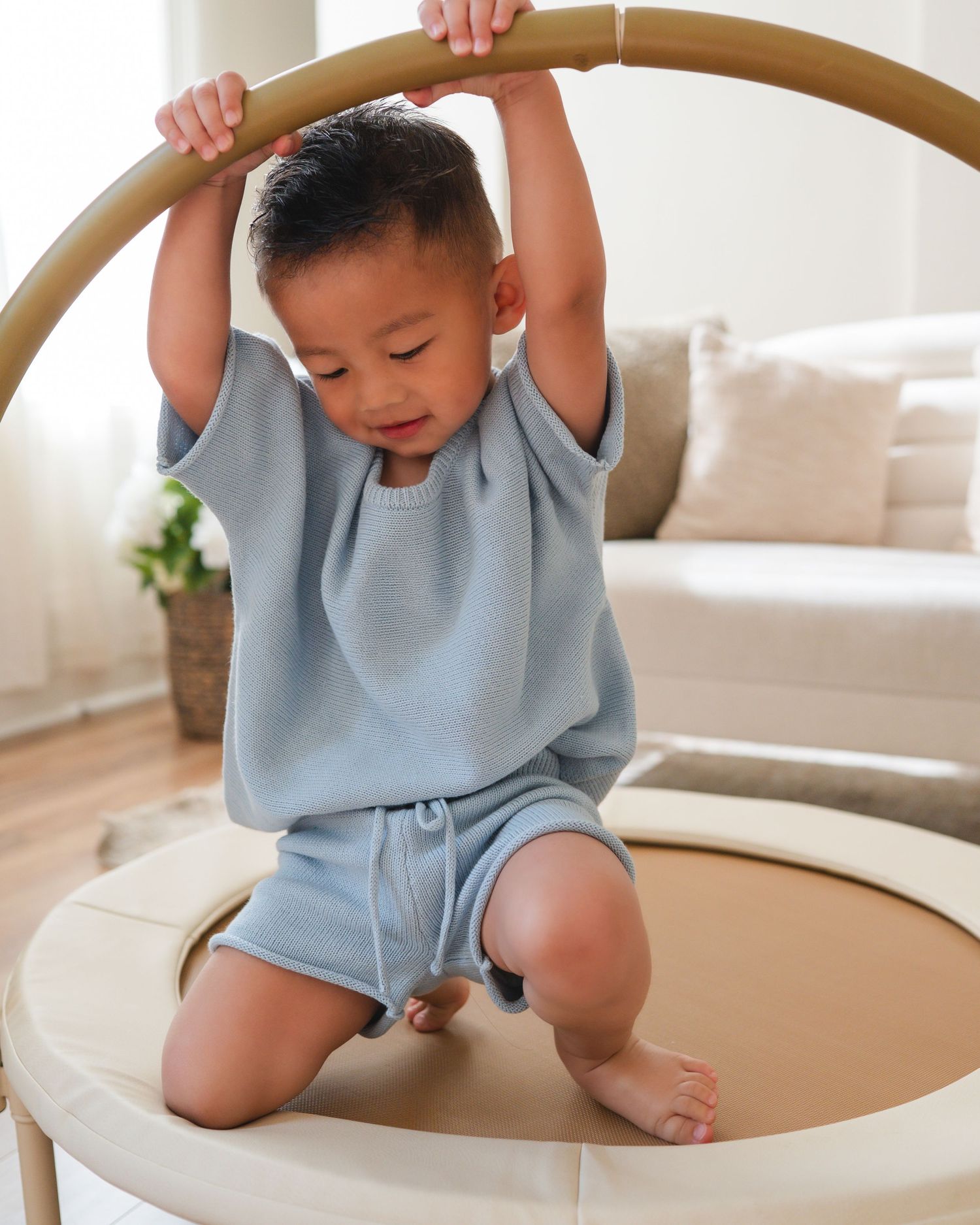 Toddler boy in blue waffle knit outfit plays on a round indoor baby gym.