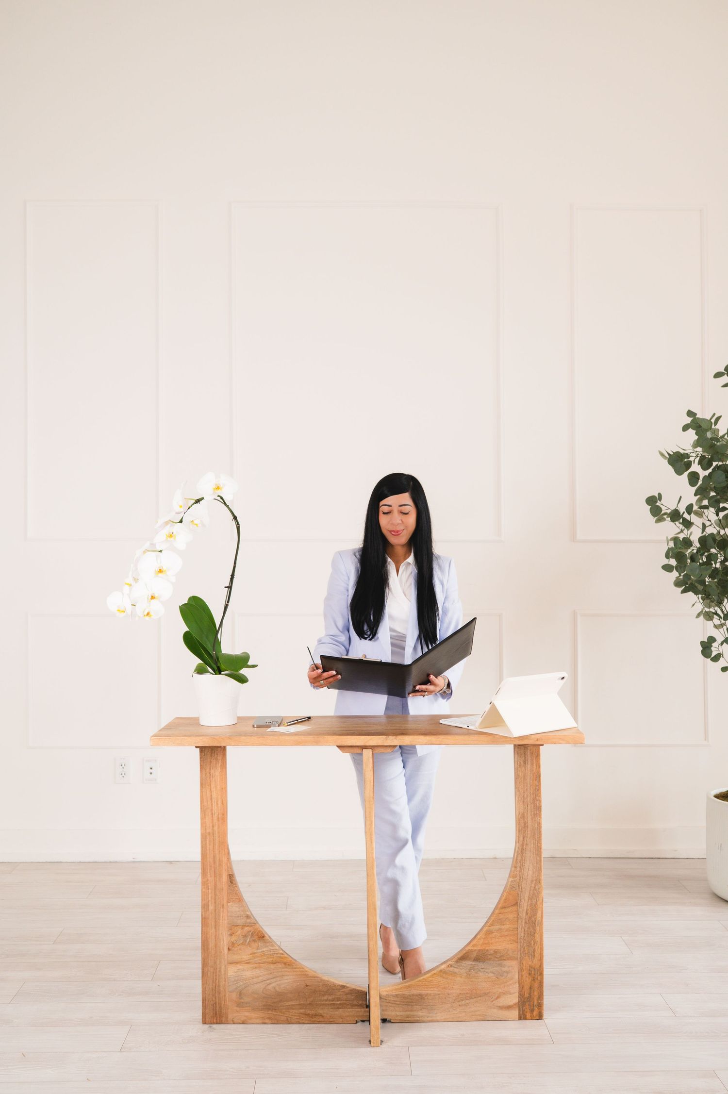 Woman in blue suit standing at wooden desk in bright white minimalist office.