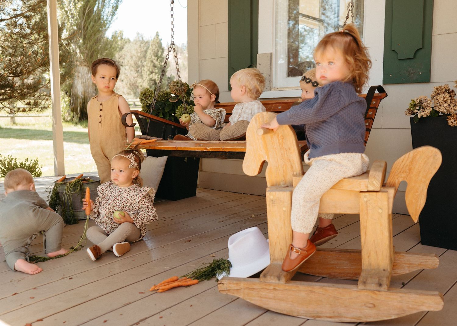 Several young children playing on a wooden porch with a natural wood rocking horse toy.