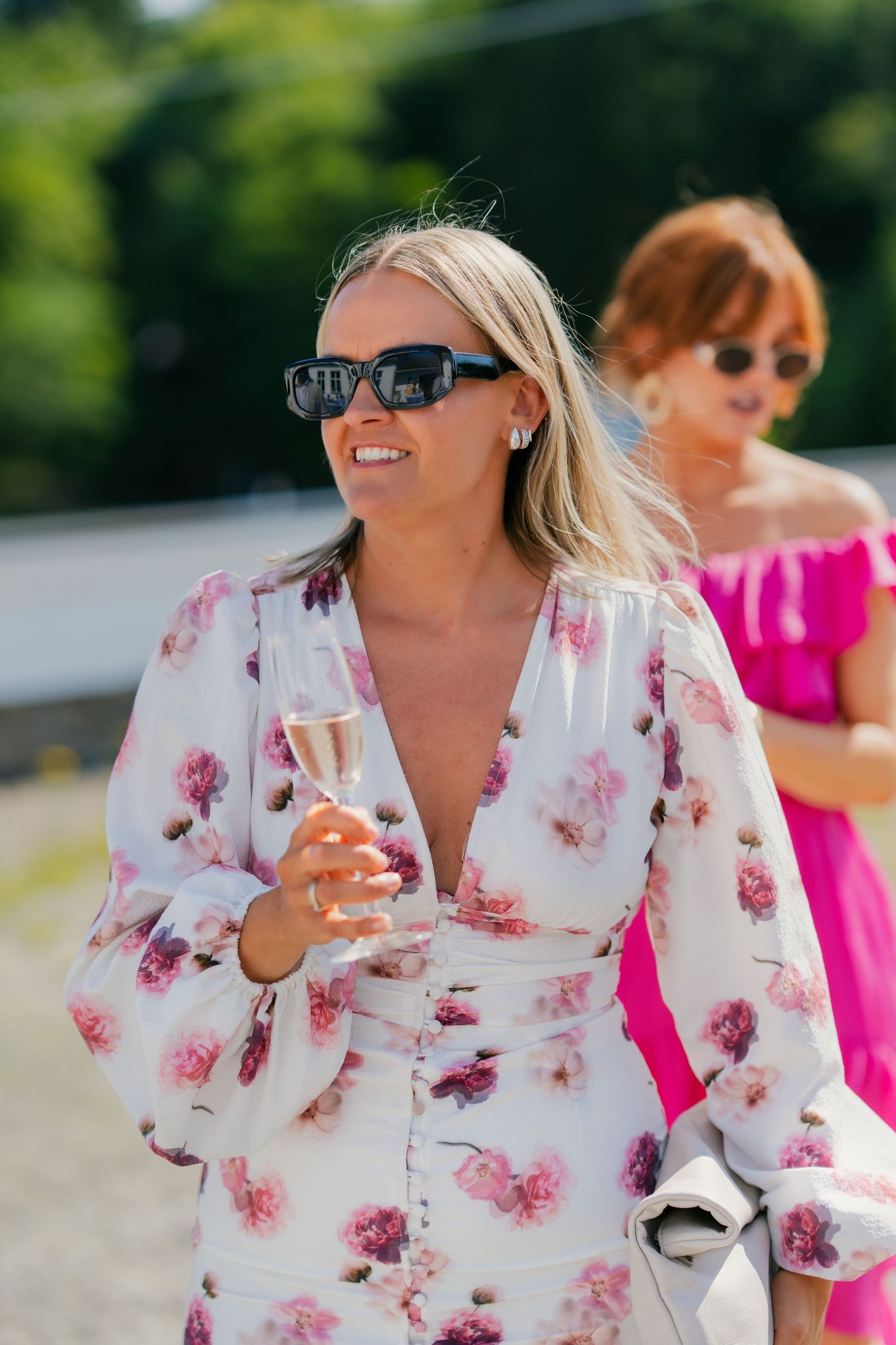 Group enjoying drinks outdoors in floral and pink attire on a sunny day.
