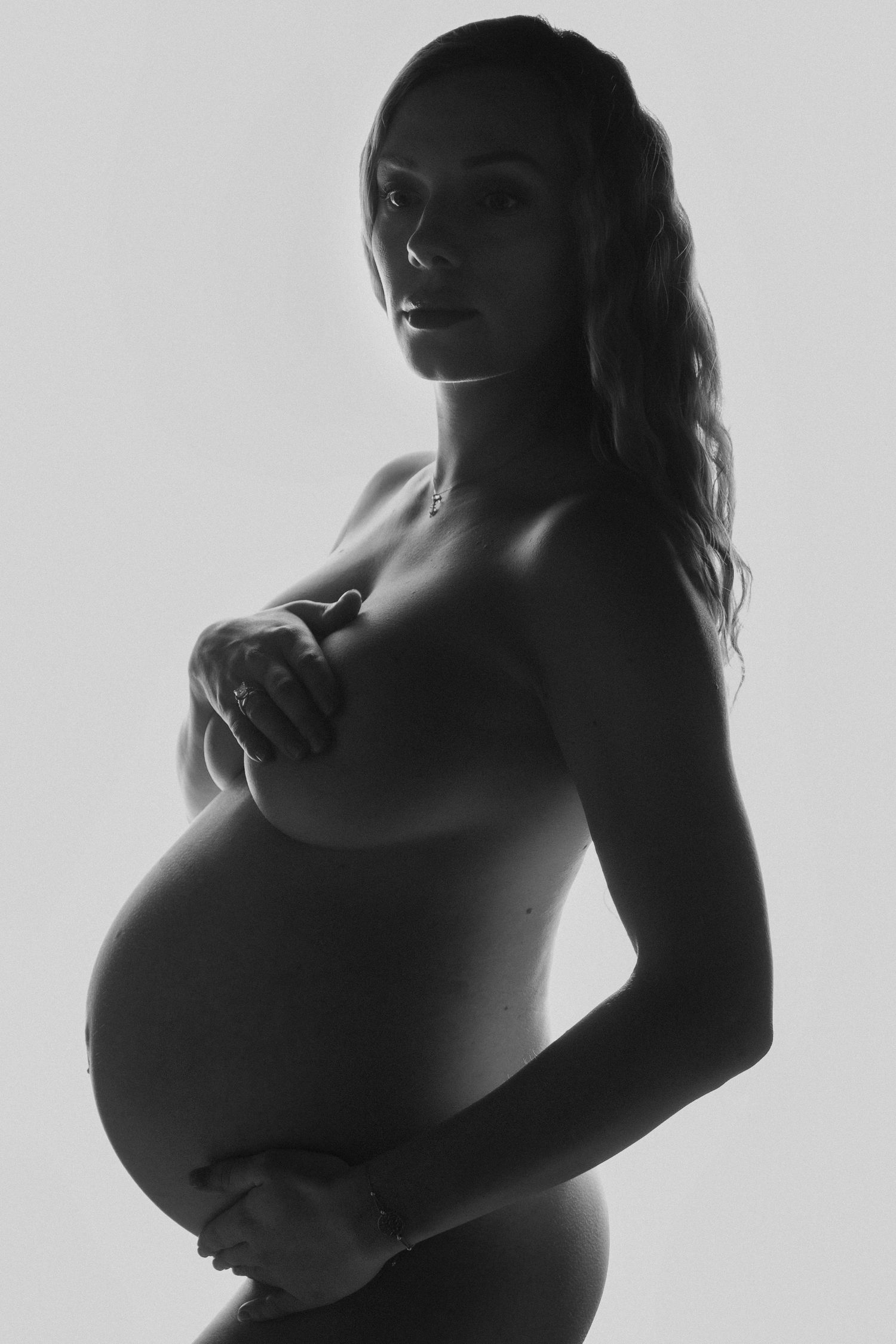 High-key maternity photography series showing side profile of pregnant figure.
