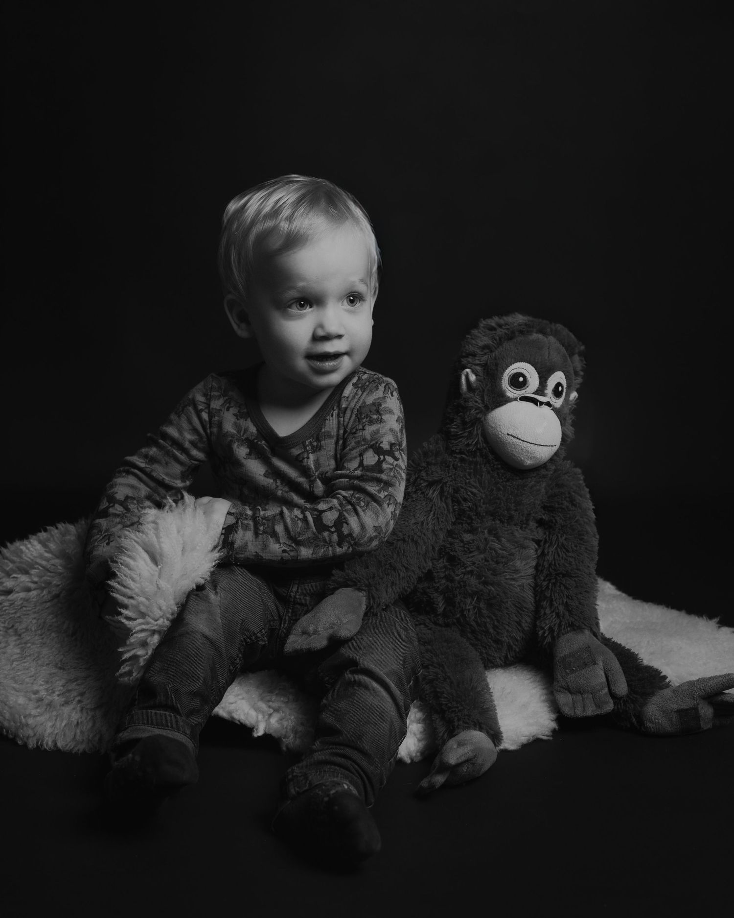 Toddler playing with stuffed animals in moody black and white portrait.
