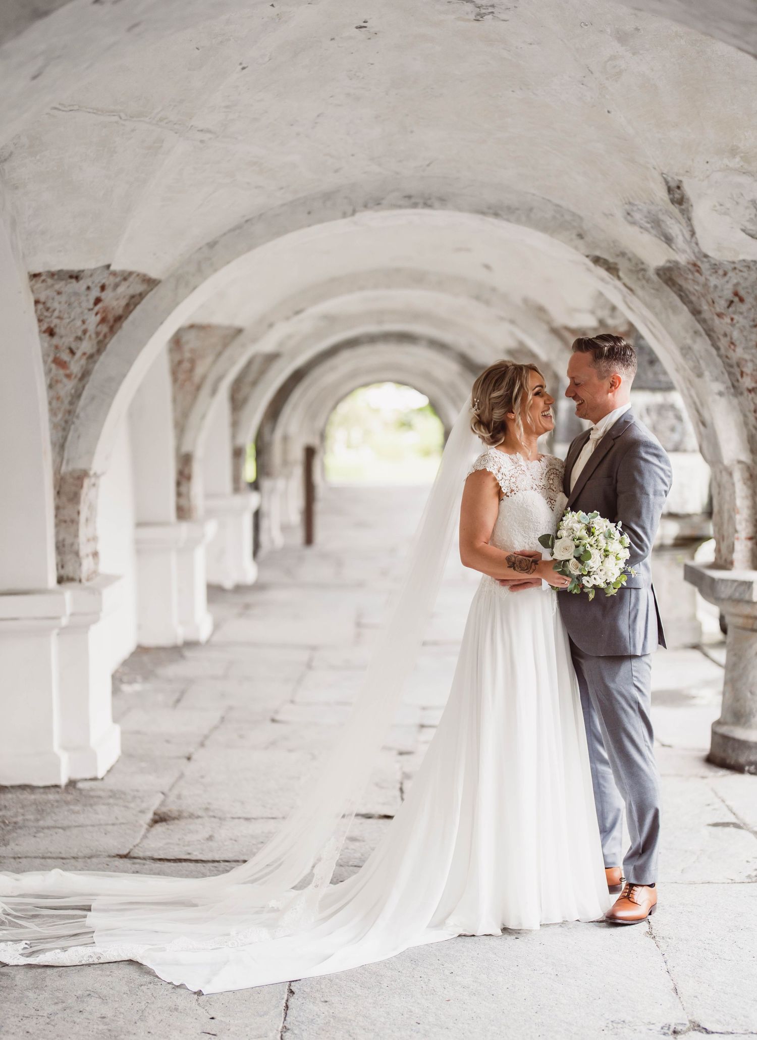Romantic wedding portraits under white stone archways with dramatic lighting.