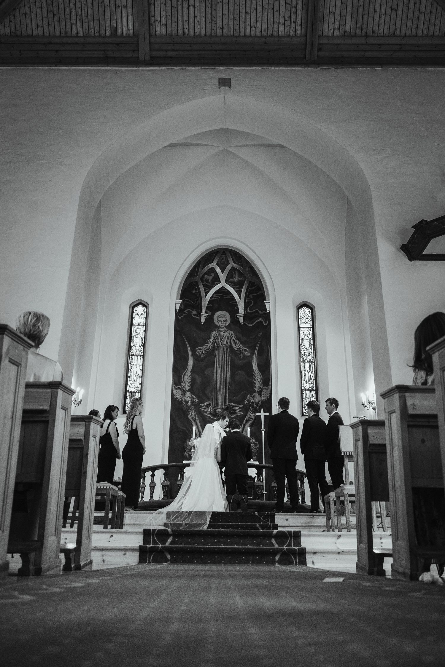 Black and white interior shot of a church ceremony with vaulted ceilings and stained glass windows.