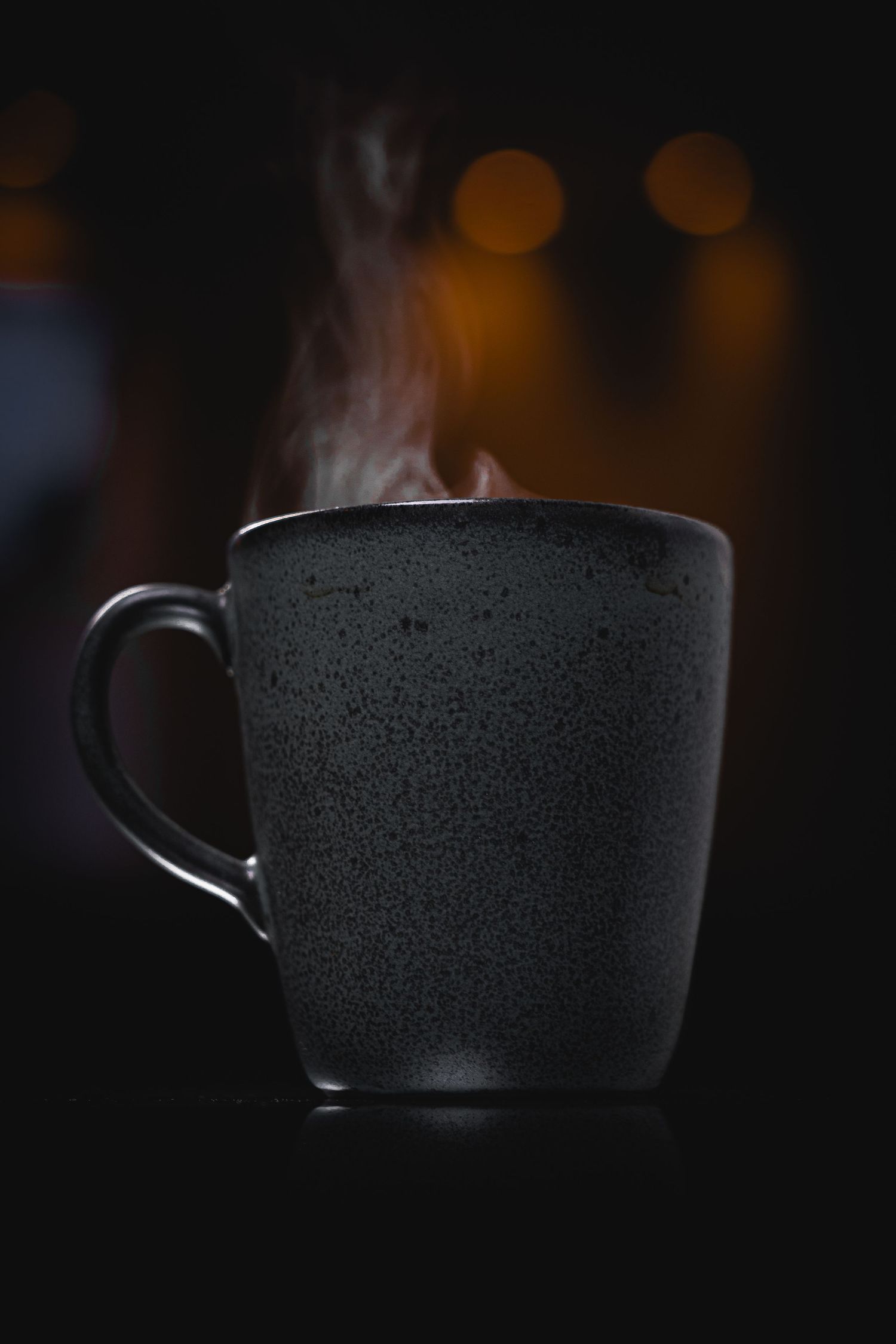Dark silhouette of a coffee cup with steam against black background.