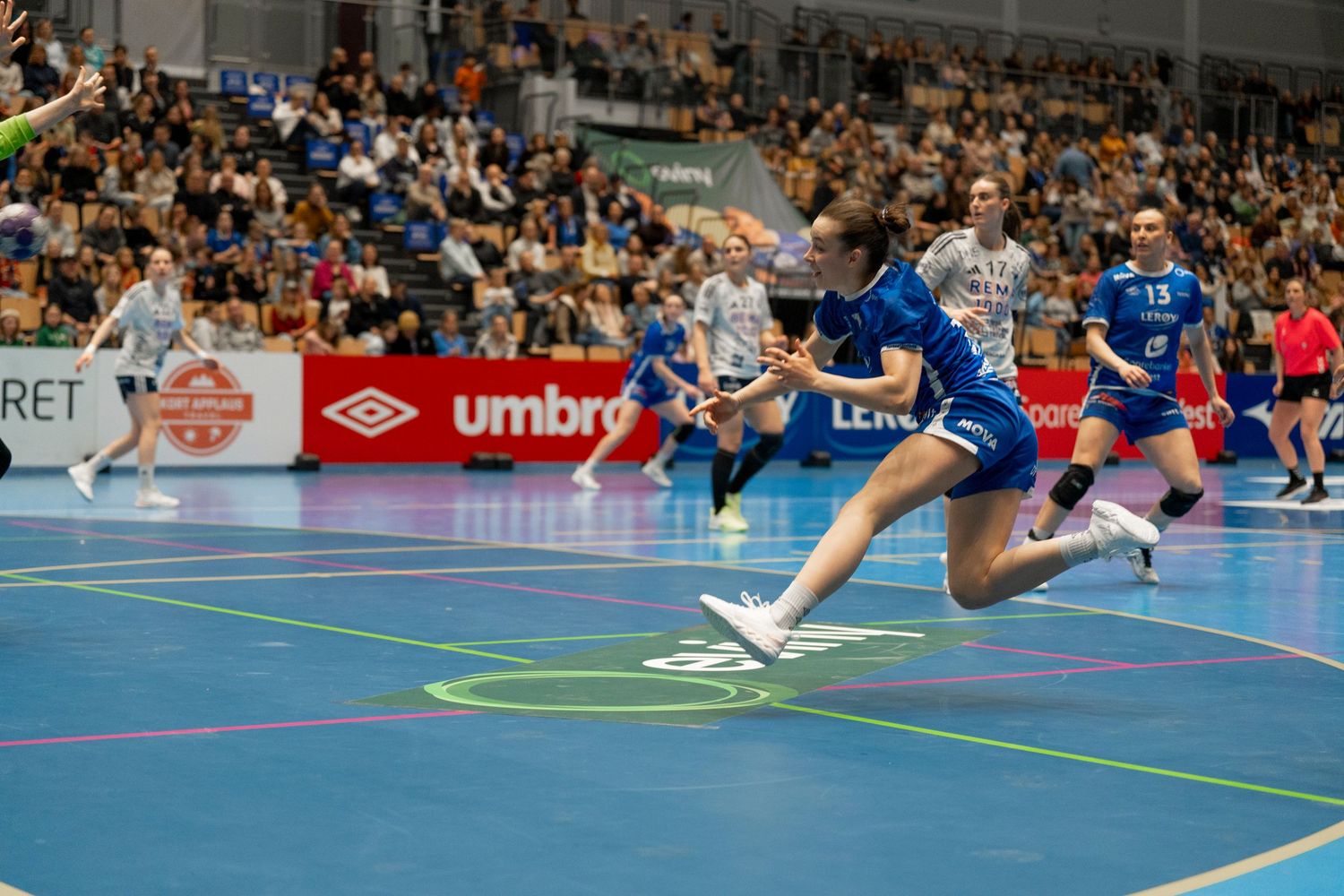 Indoor handball or futsal match with players in action on blue court.