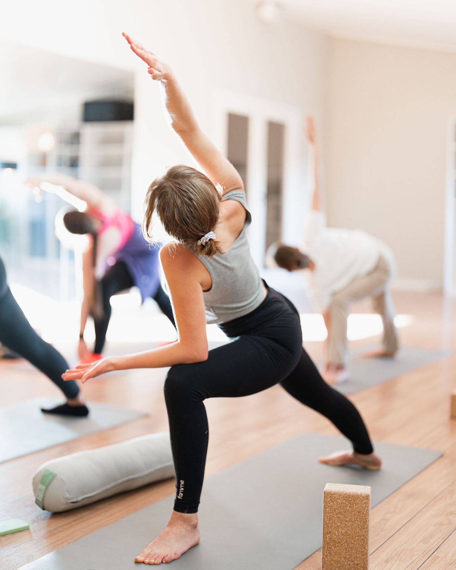 Group yoga class practicing stretching poses on yoga mats with blocks.