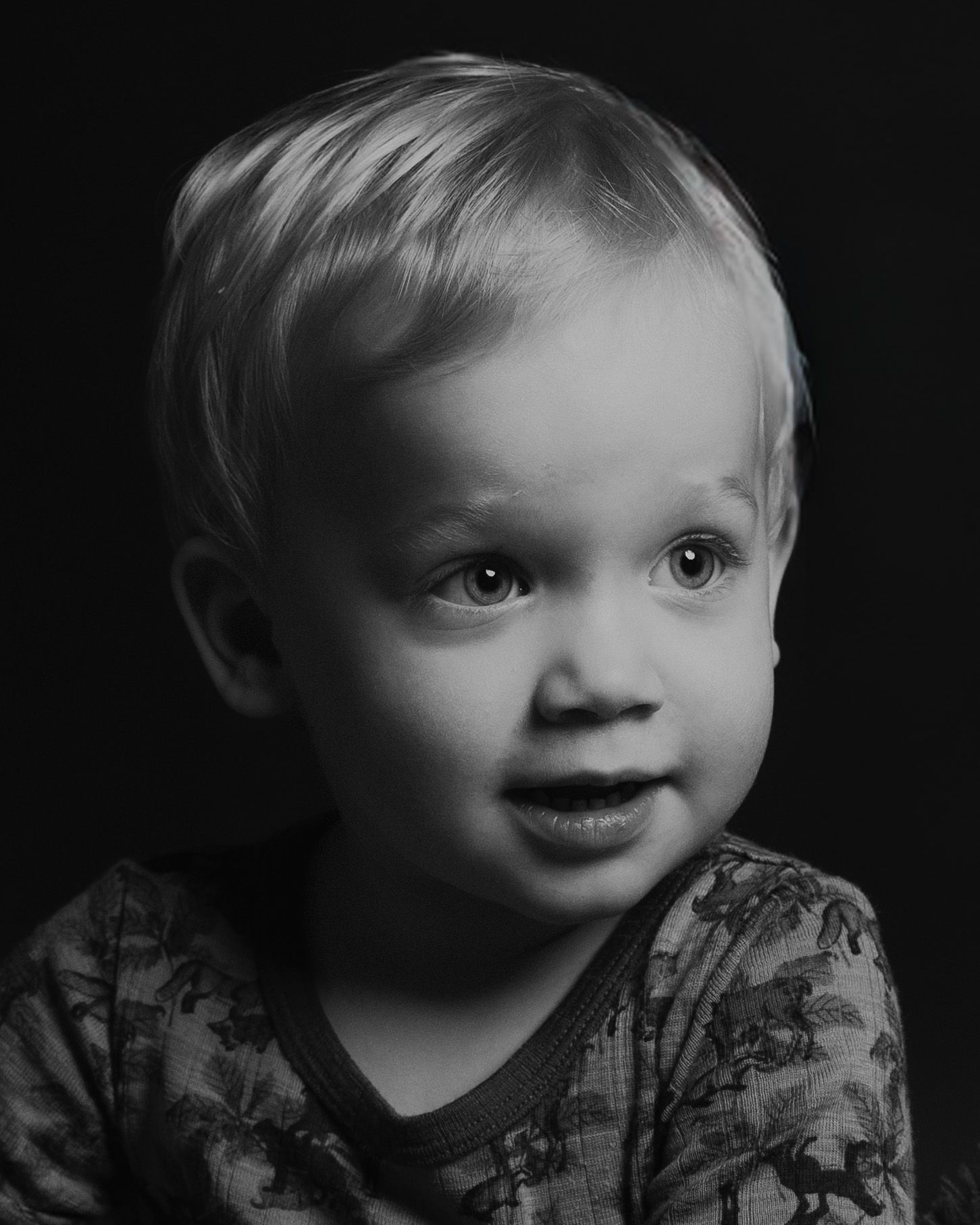 Black and white portrait of a toddler with dramatic lighting against dark background.