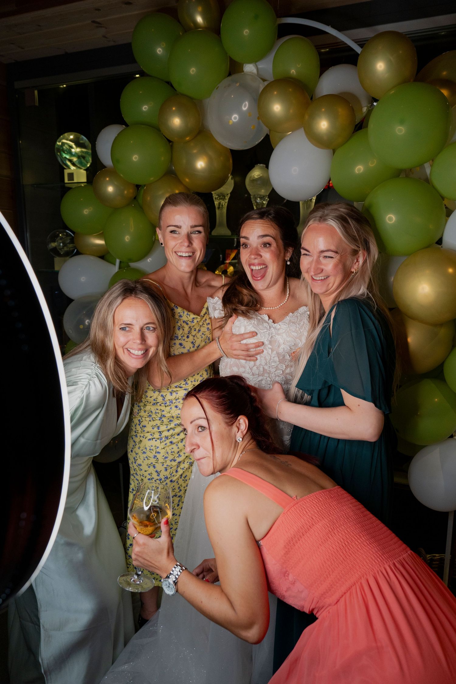 Wedding party dancing and celebrating under green and gold balloon decorations.