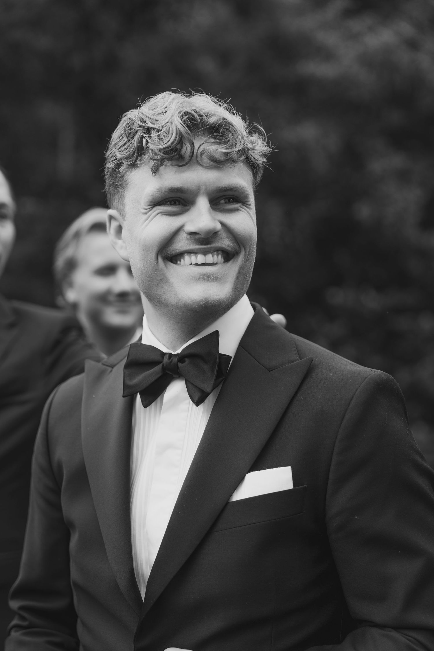 Black and white portrait of wedding party members in formal attire outdoors.