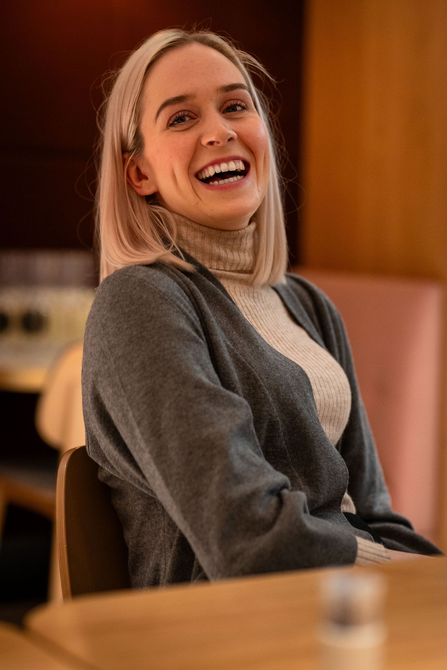 Person wearing cozy grey sweater and turtleneck sitting in warm indoor lighting.