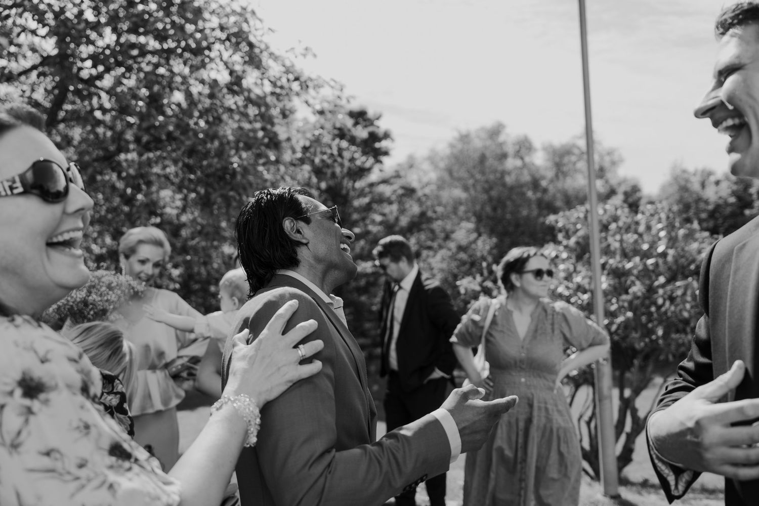 Wedding guests gather outdoors for celebratory photos in natural lighting.