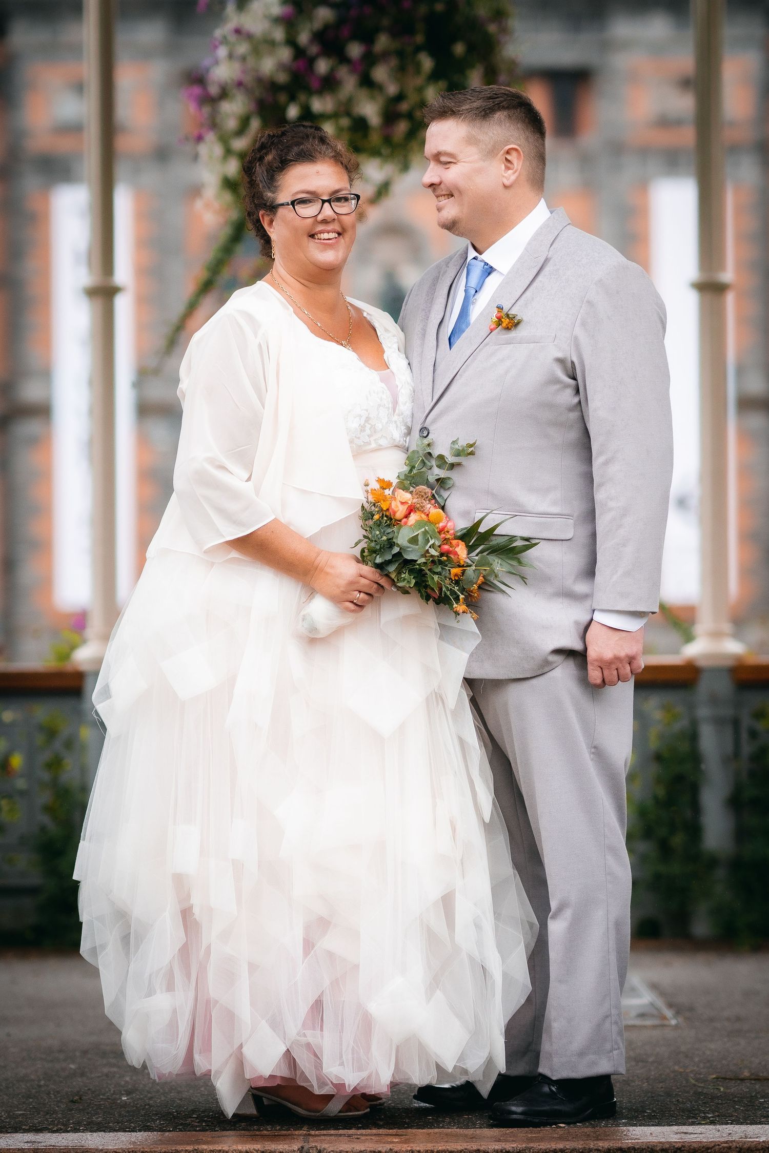 Couple in white and grey wedding attire sharing a joyful moment outdoors.