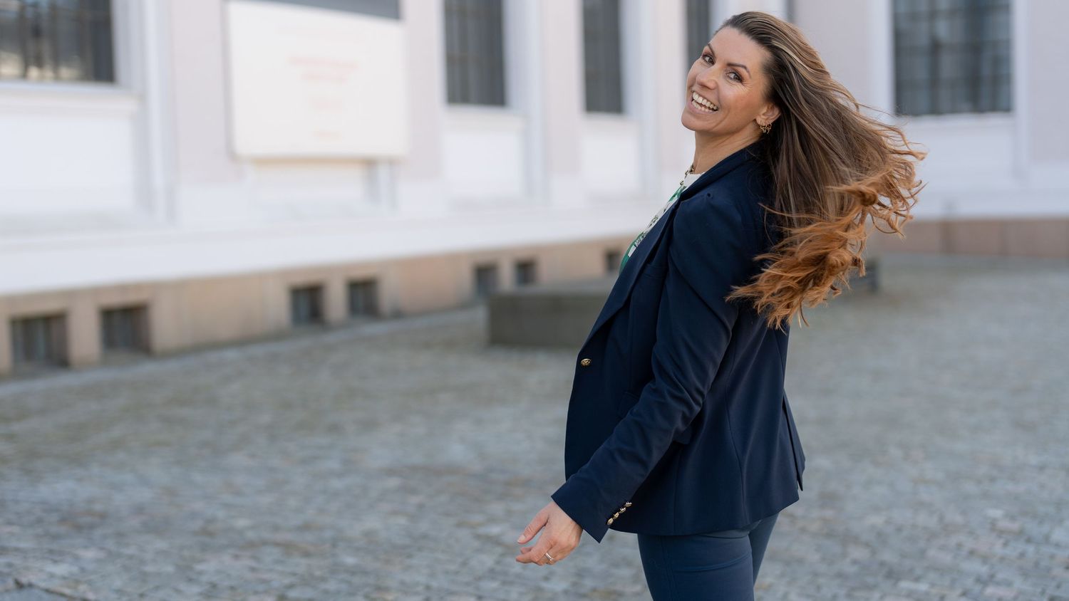 A person with long hair running joyfully outdoors in casual attire.