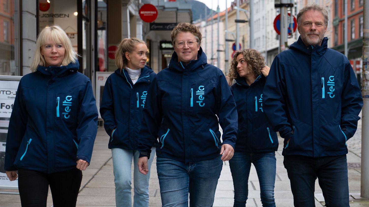 Group of people walking down a street wearing matching navy blue jackets.