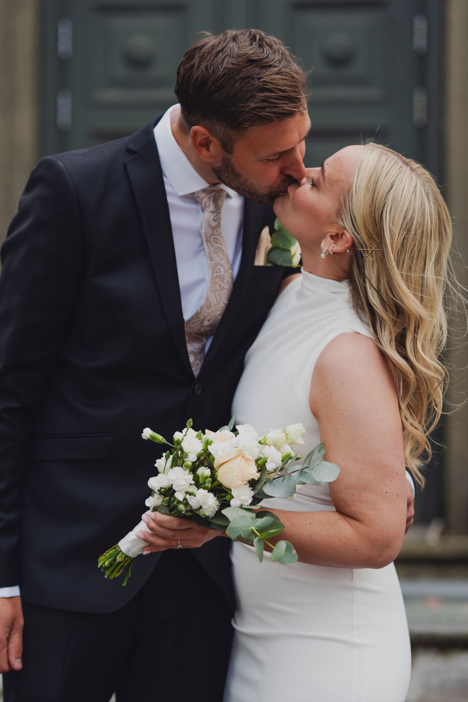 Couple sharing intimate moment with white floral bouquet during wedding portraits.