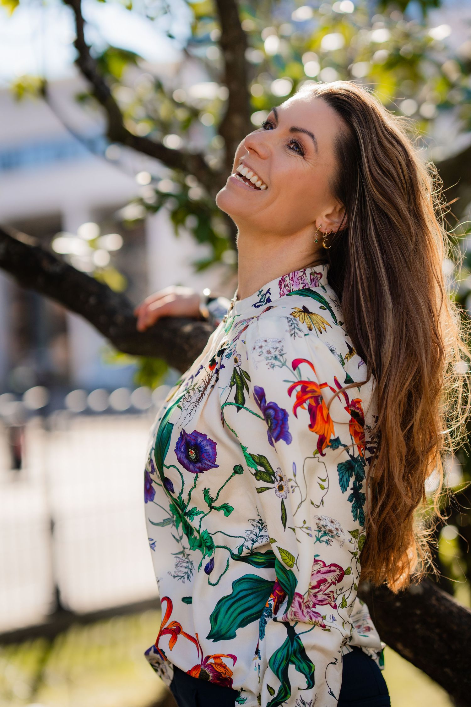 Someone wearing a floral print blouse poses playfully under tree branches.