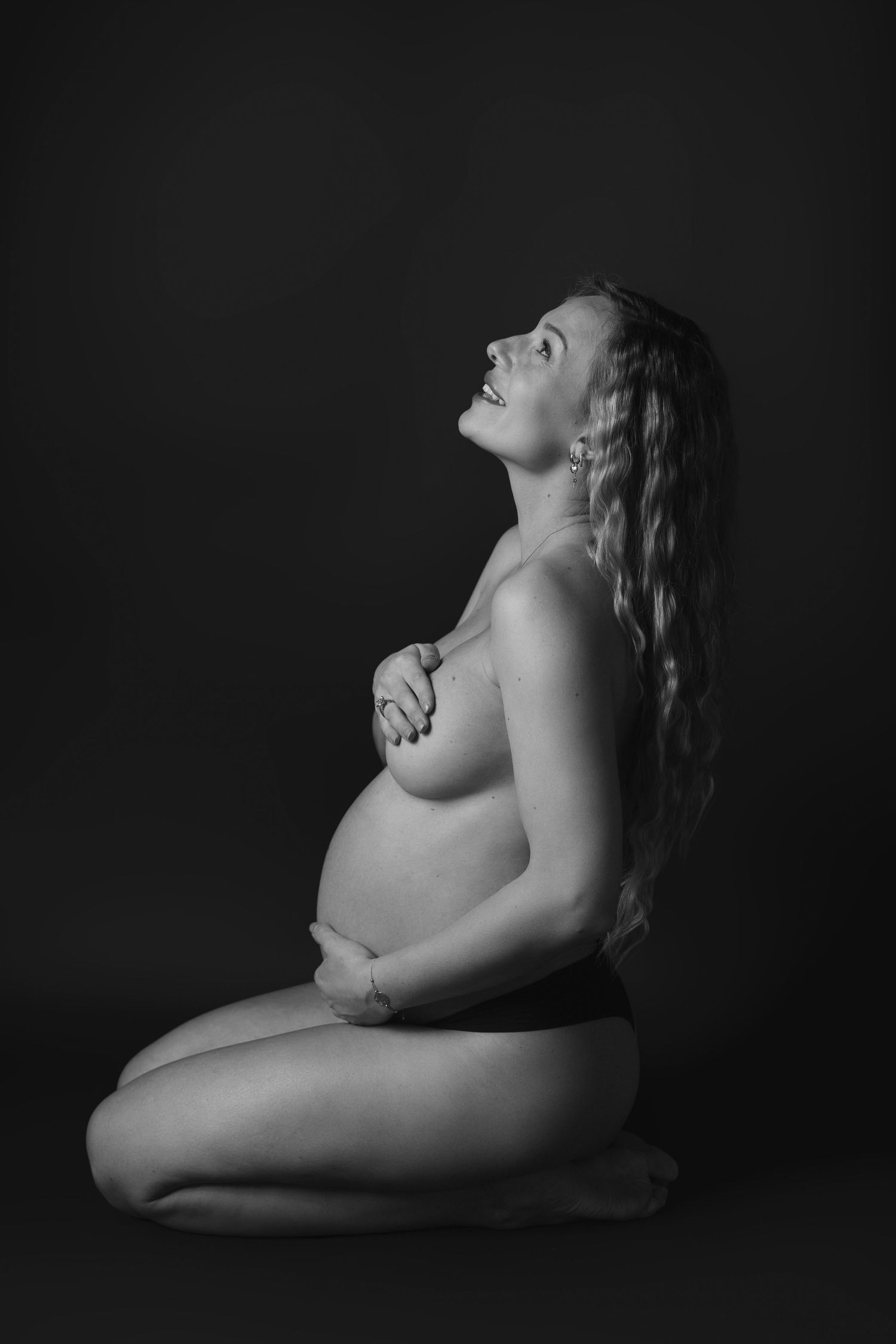 Artistic nude maternity portrait in black and white with dramatic shadows.