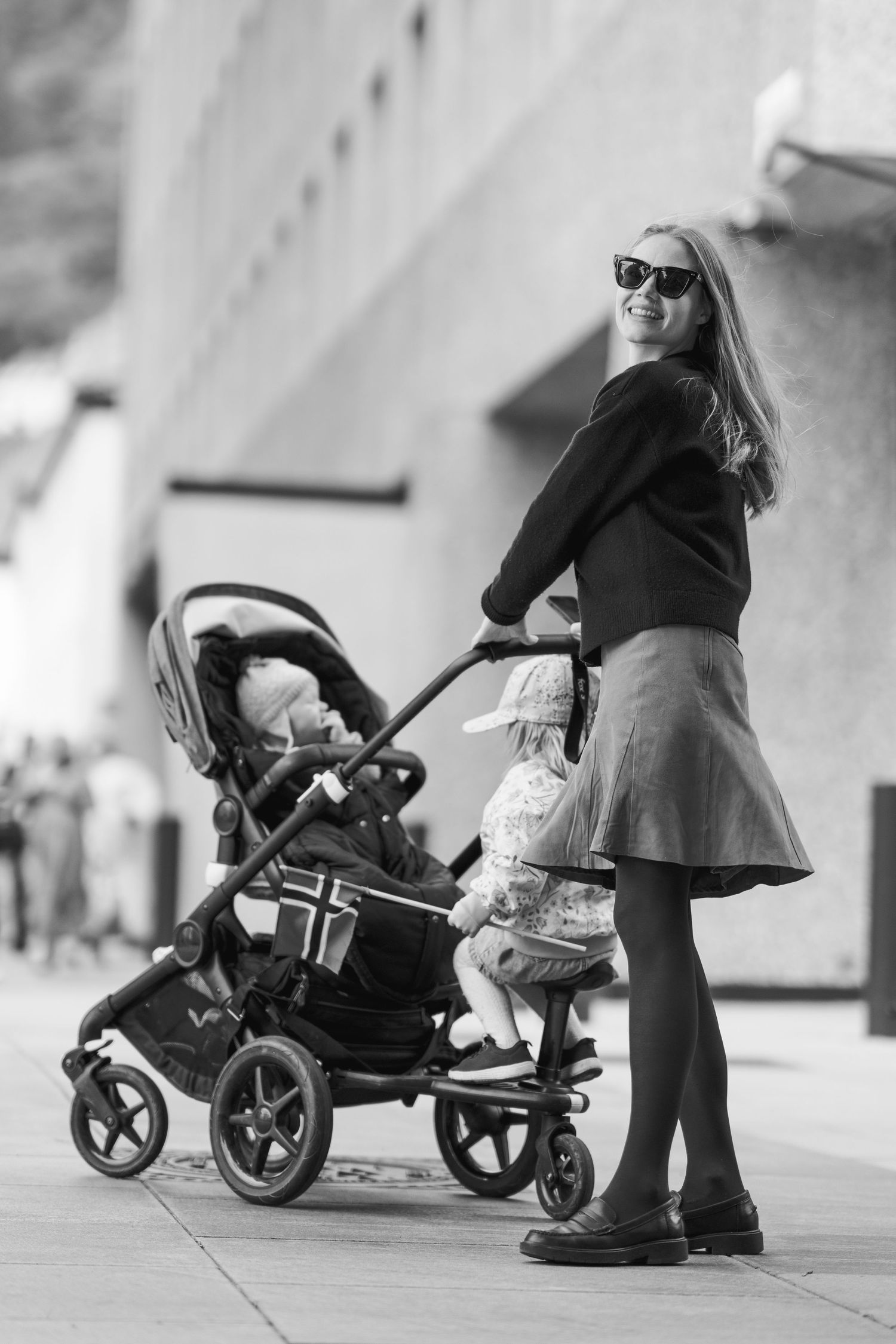 Black and white sequence of strollers moving along a sidewalk in an urban setting.