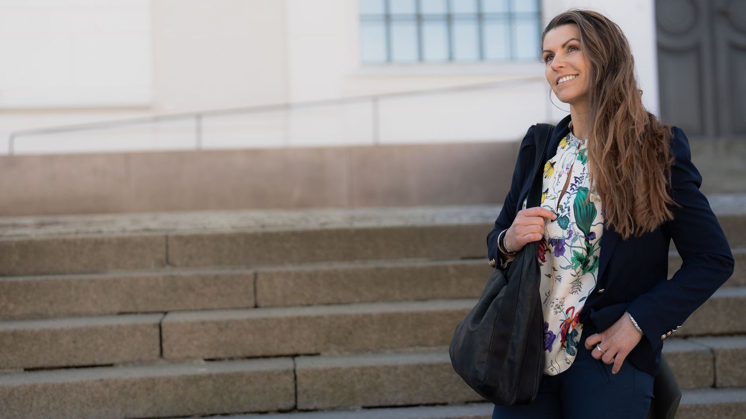 Person walking along stone steps wearing a navy blazer and floral print top.
