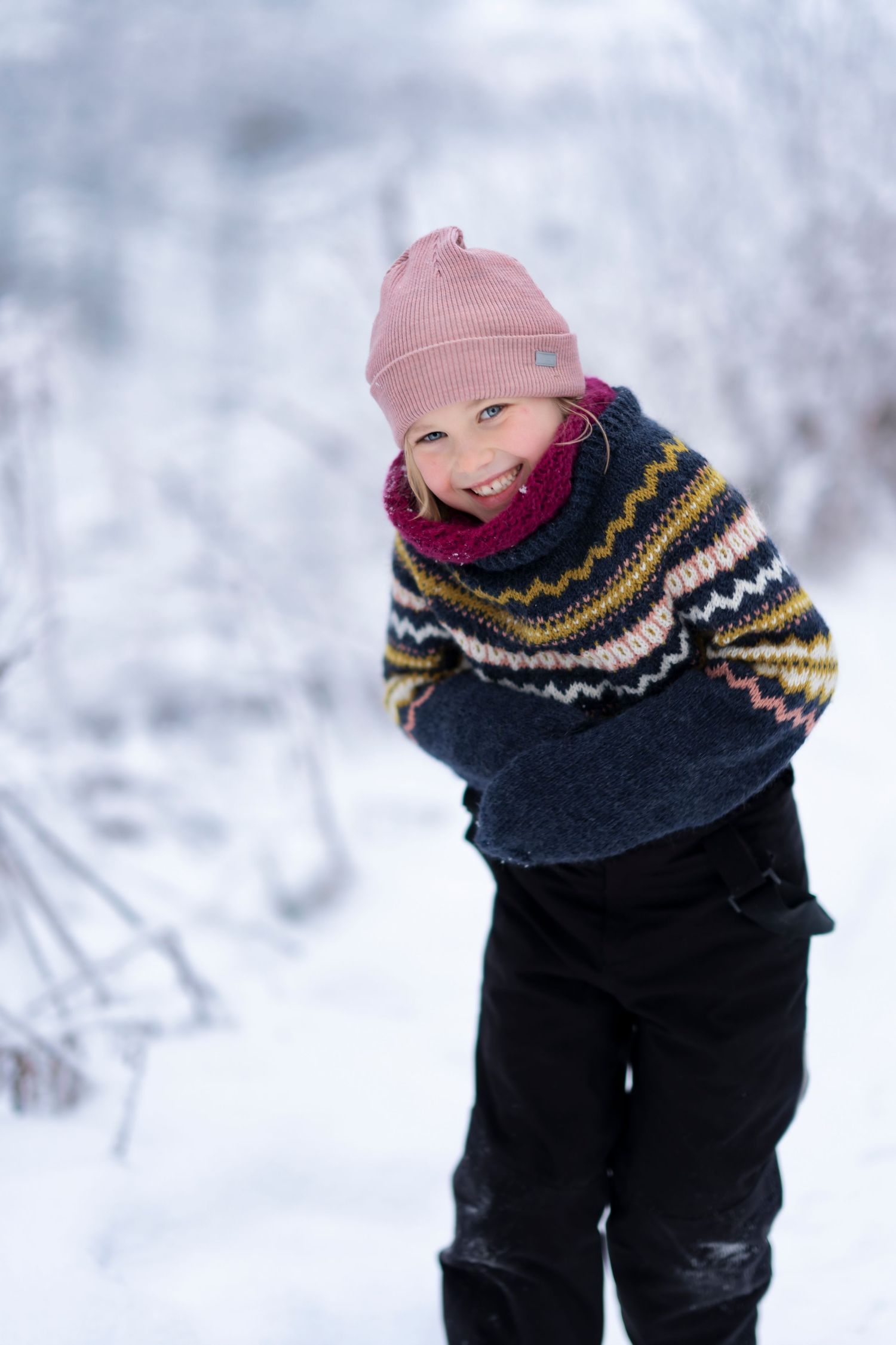 A person wearing a pink winter hat and patterned sweater plays in deep snow.