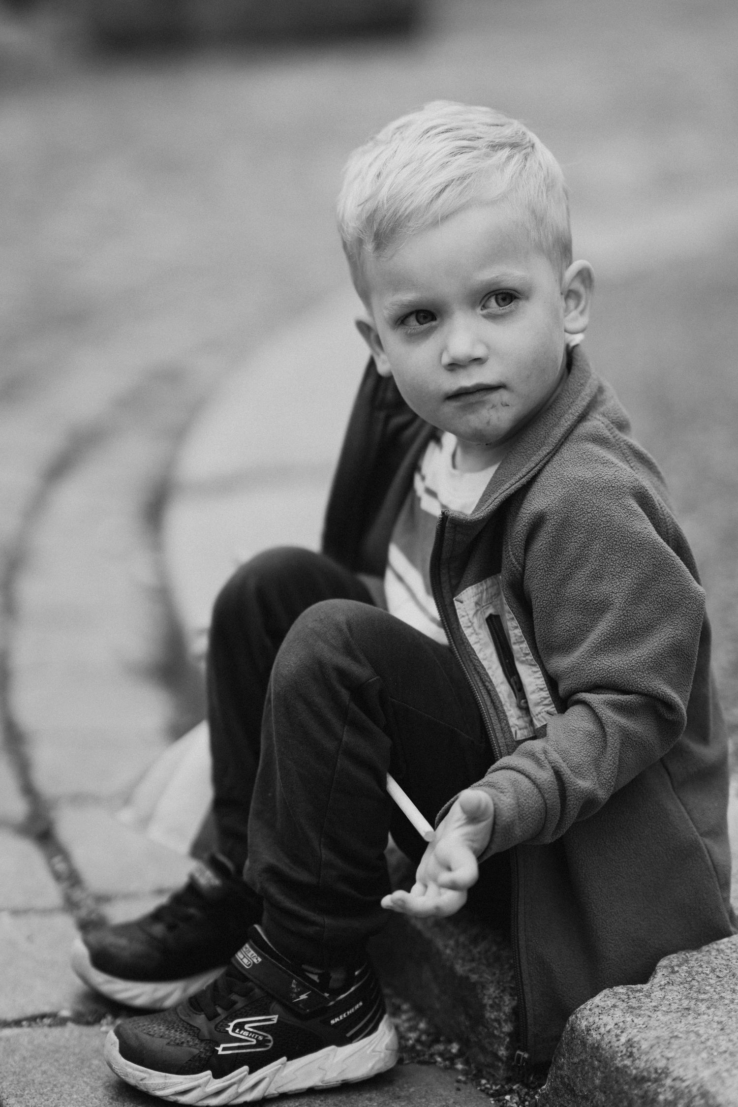 Black and white image of small child sitting on textured ground surface.