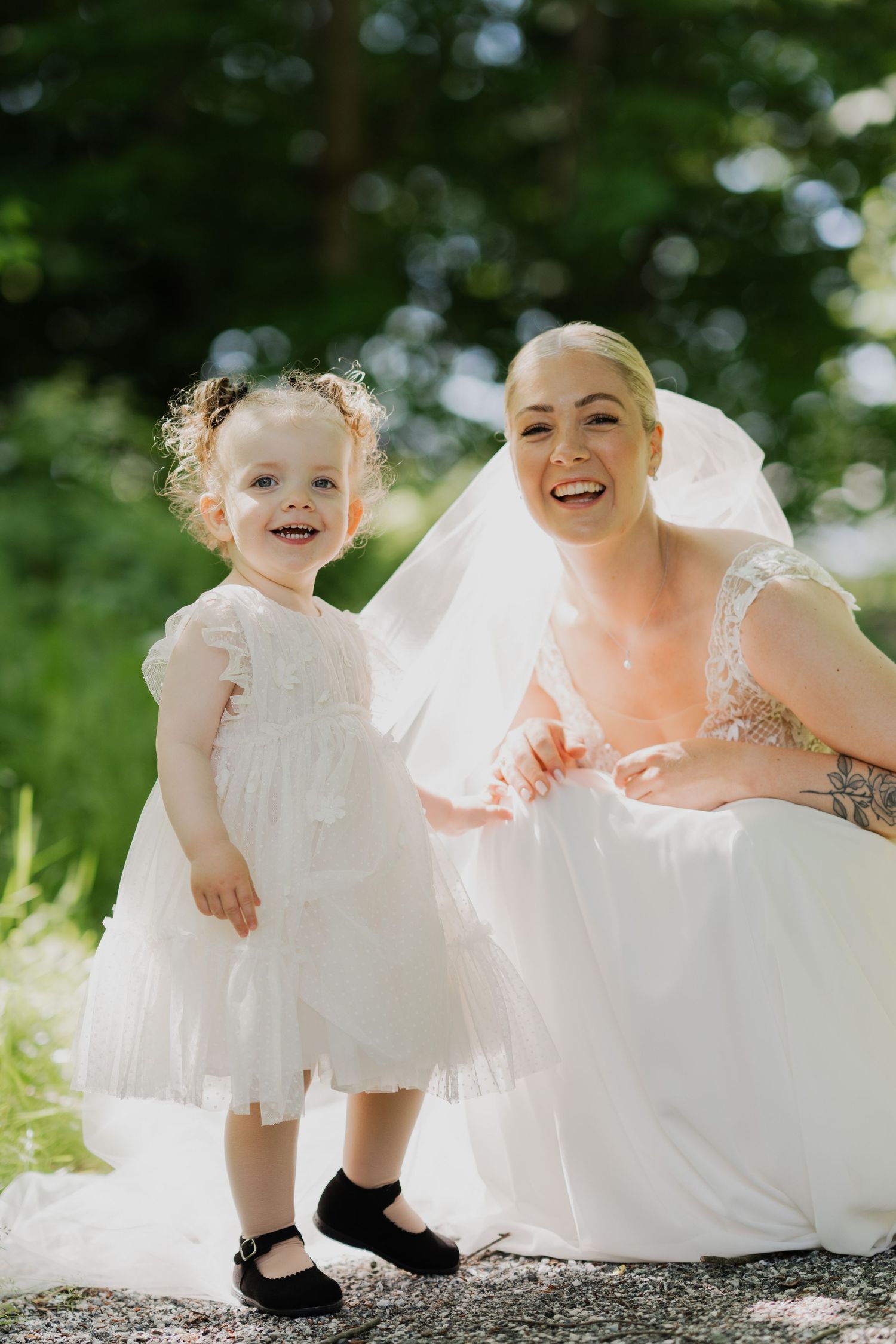 A joyful moment captured between a bride and flower girl in white dresses outdoors.
