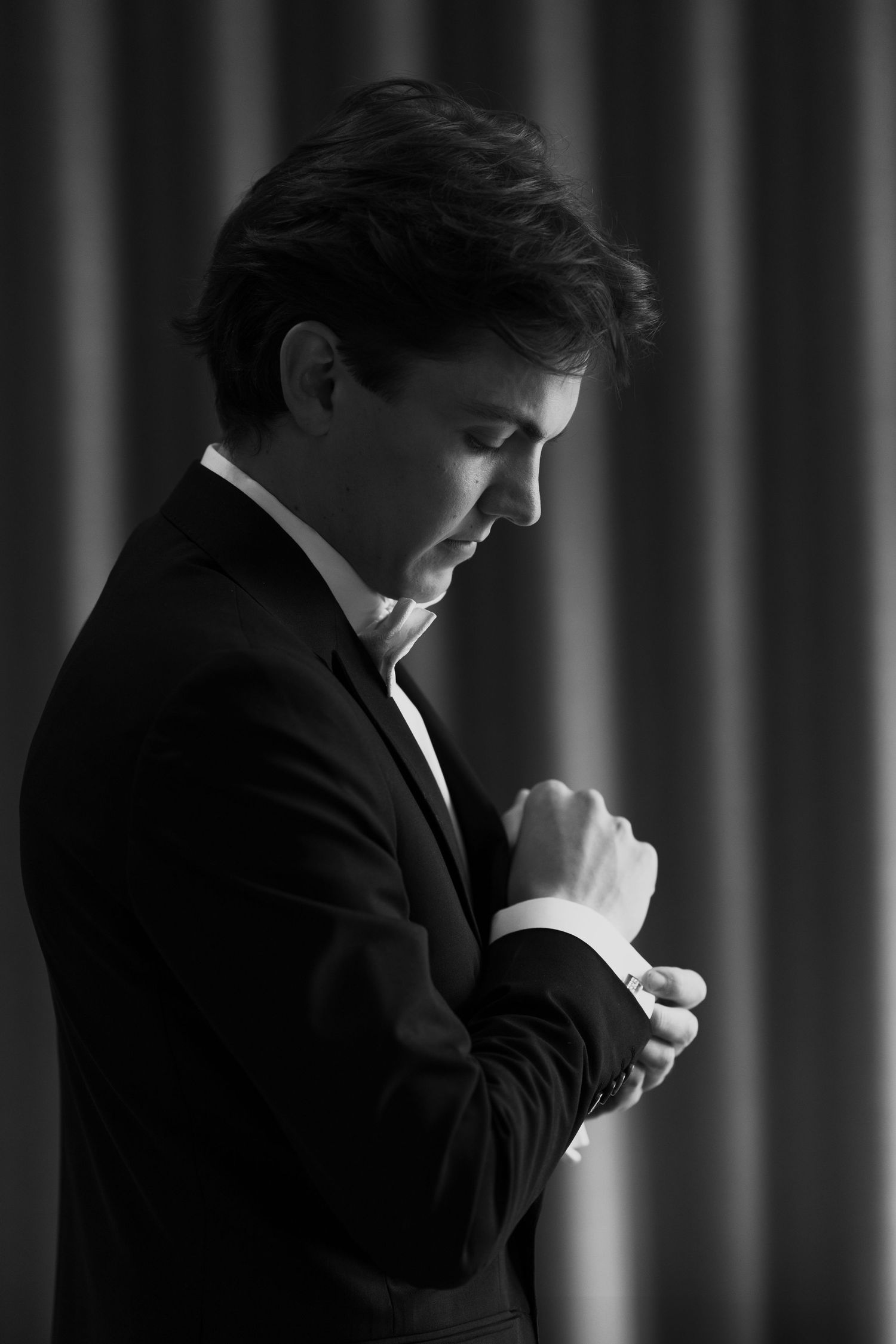 Moody portrait of a groom in formal attire with dramatic shadows and lighting.