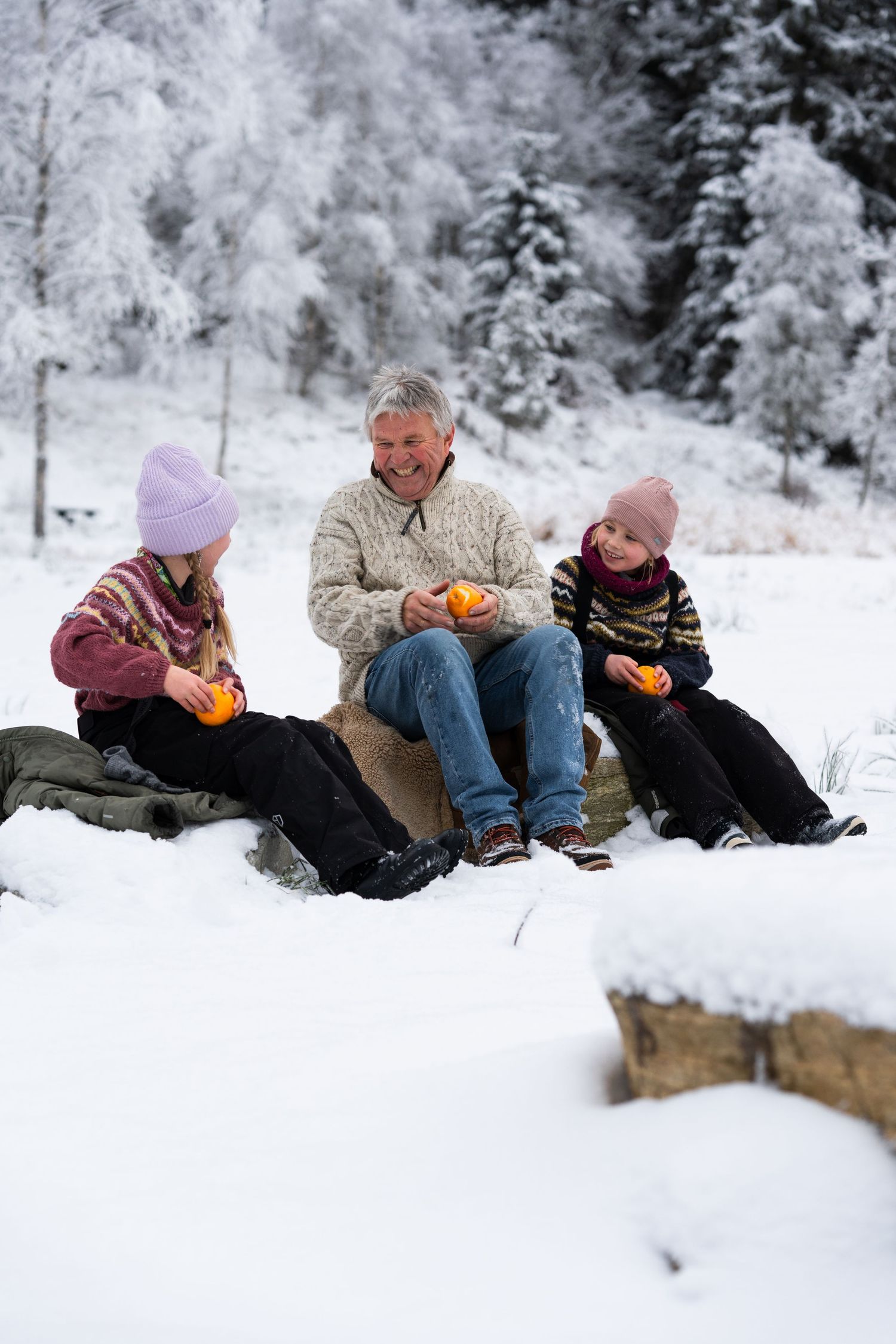 People relaxing together in snow while sharing oranges.