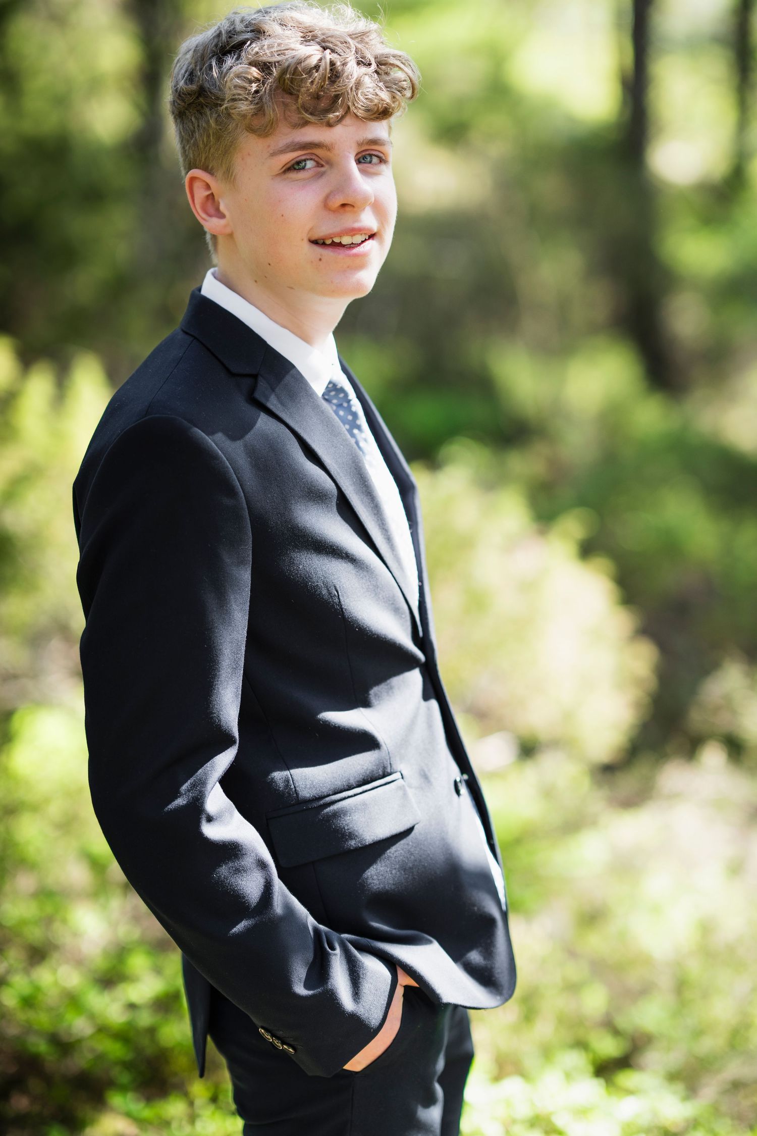 Candid outdoor photography showing various poses in a dark suit against a sunlit natural background.