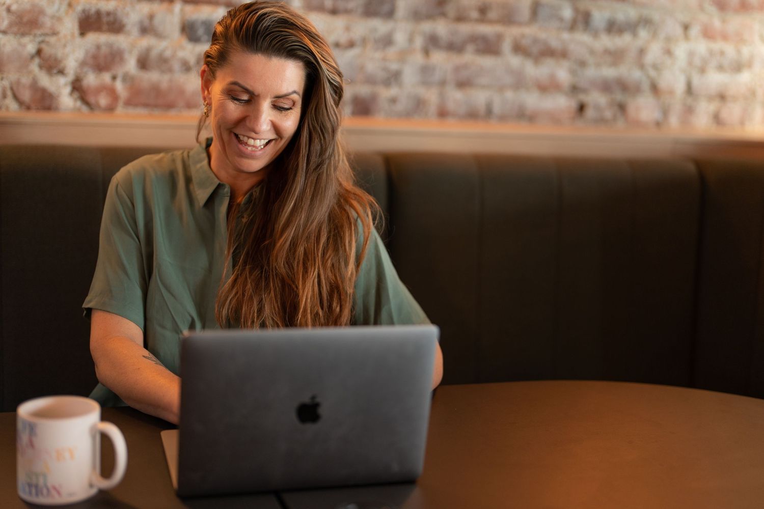 Person working on MacBook laptop in casual setting with exposed brick wall background.