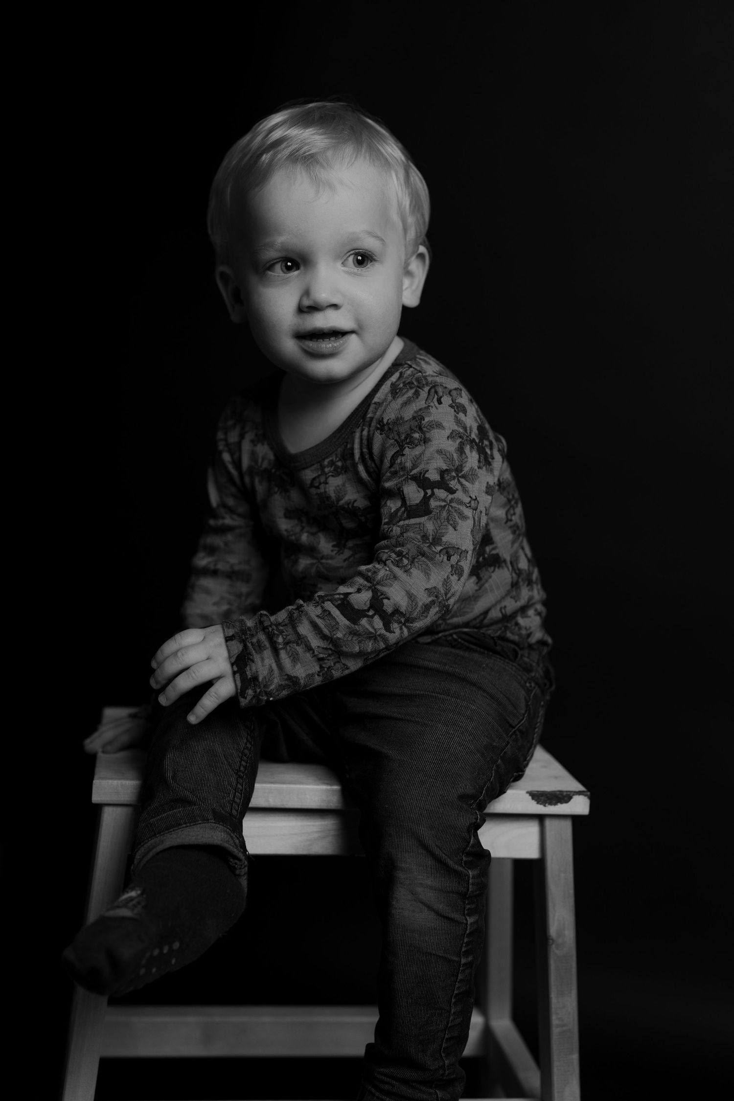 Child sitting on white chair in black and white artistic photo.