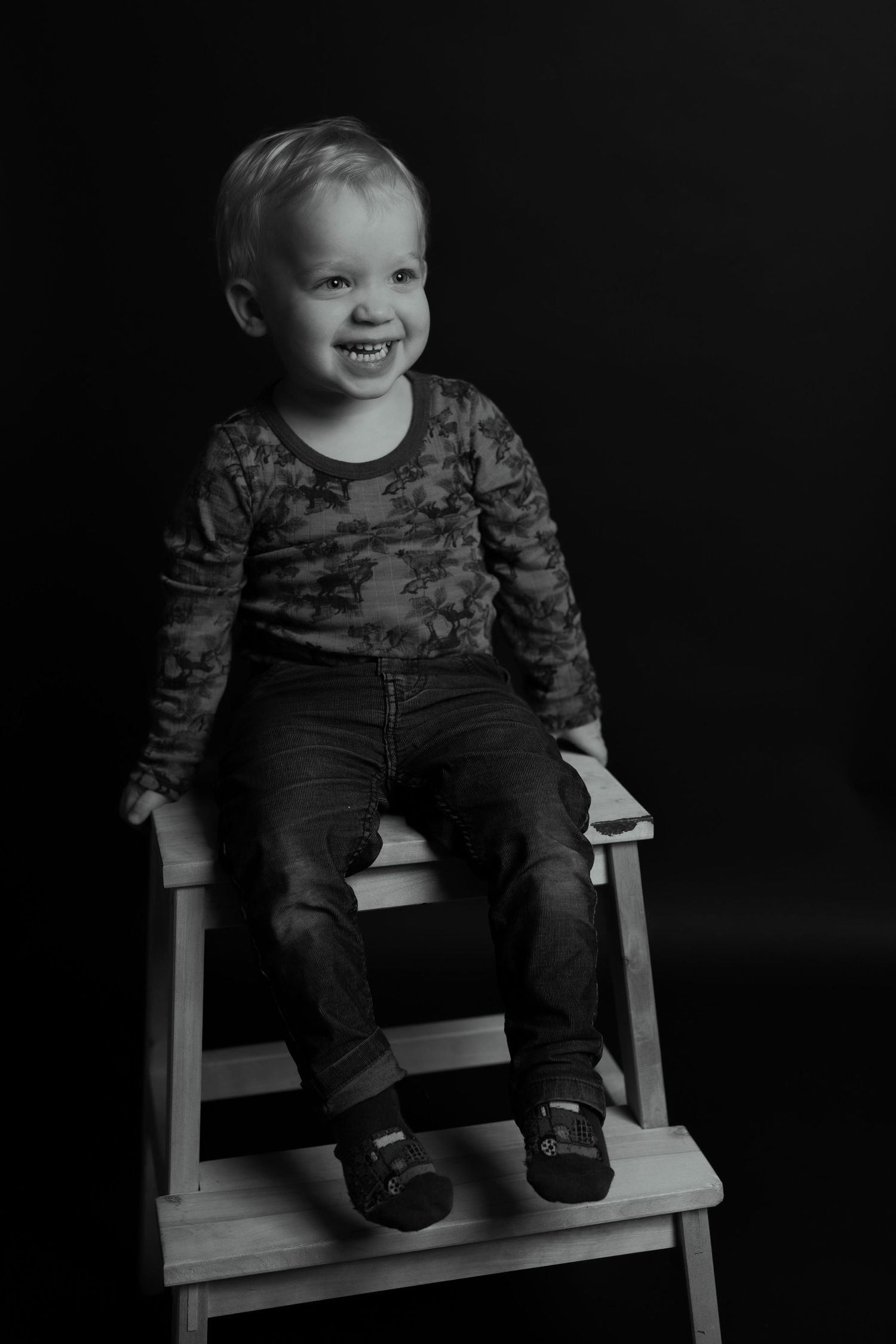 Child sitting on white wooden steps in dramatic black and white photography.