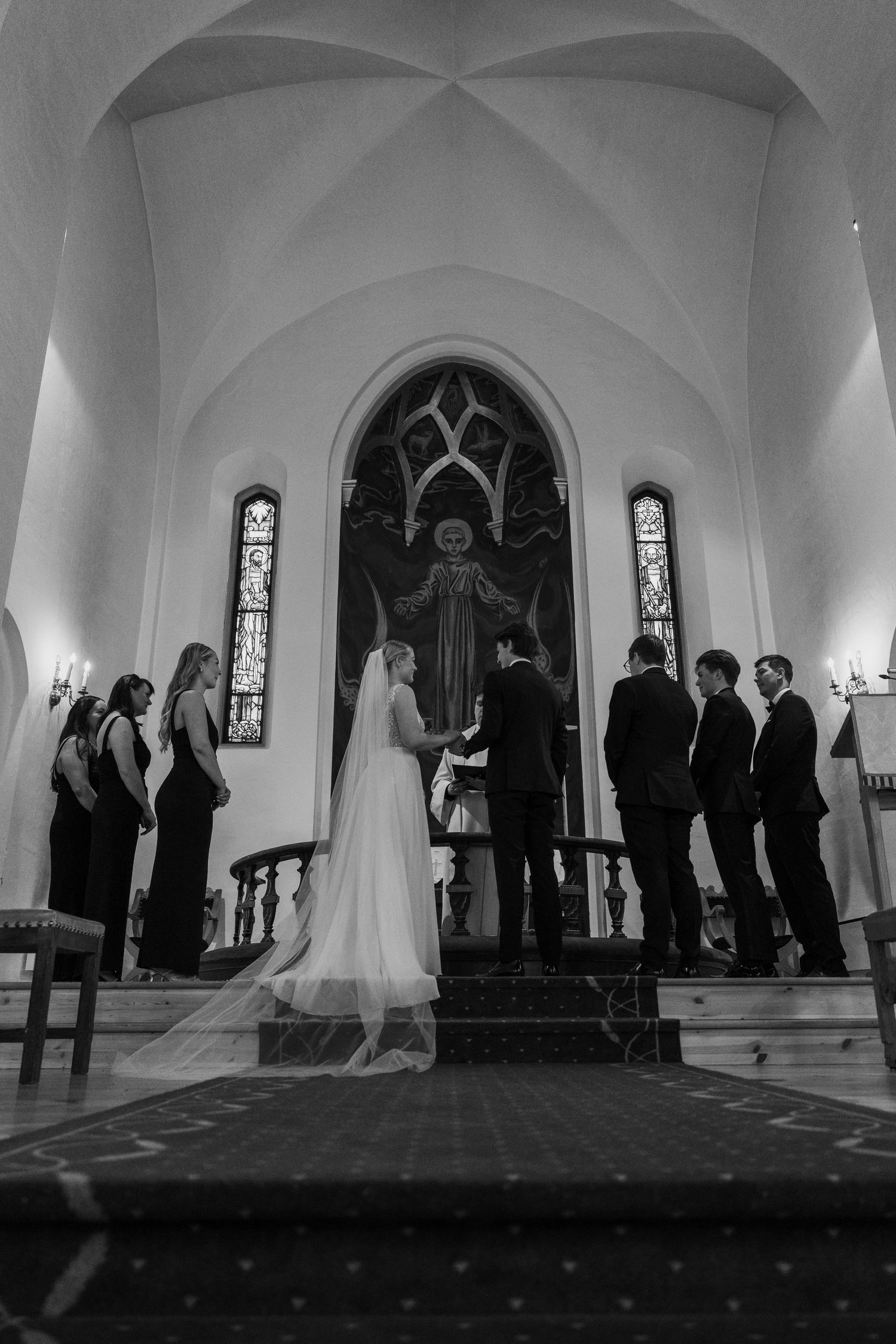 Wide angle view of a church wedding ceremony with silhouettes of guests against white arched walls.