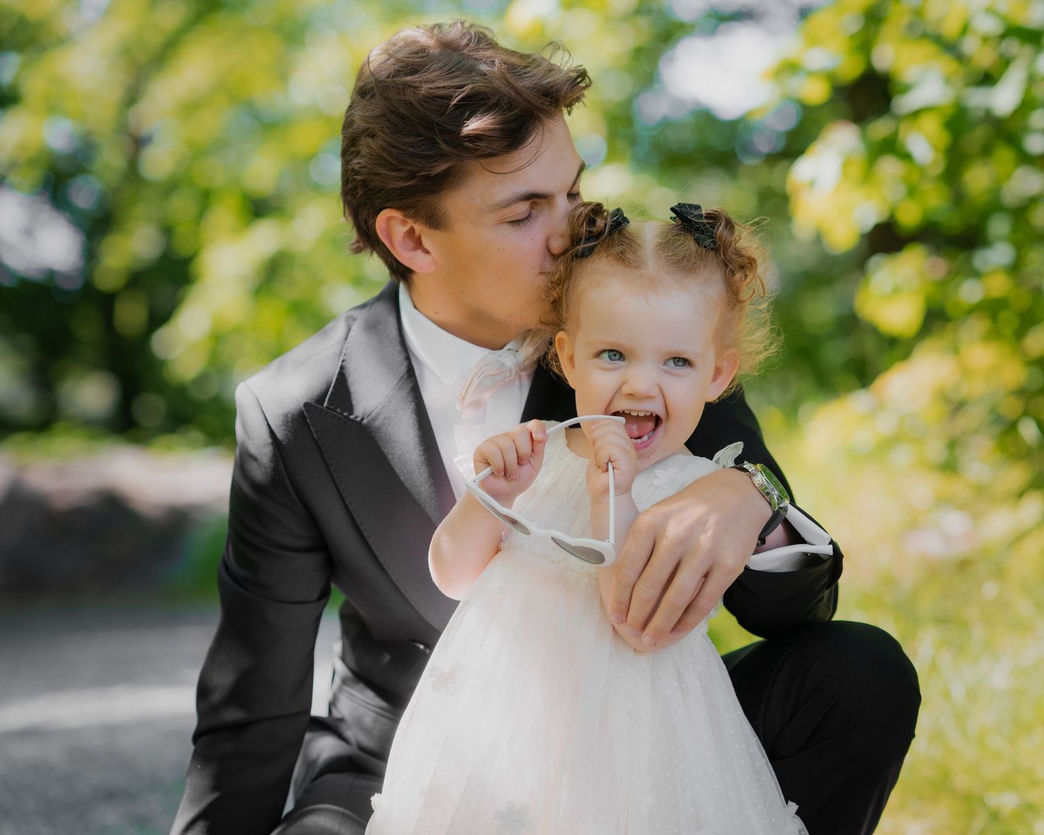 Wedding couple embraces outdoors with soft natural lighting and green foliage in the background.