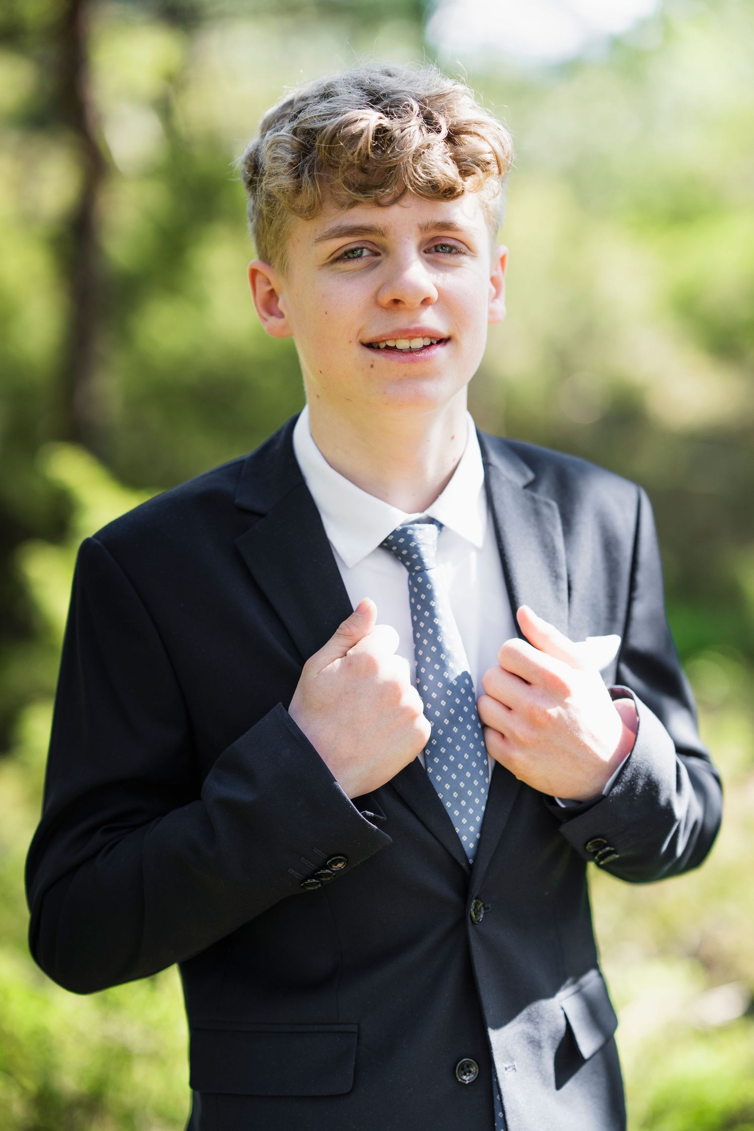 Outdoor formal portraits showing someone adjusting their tie against a blurred natural background.