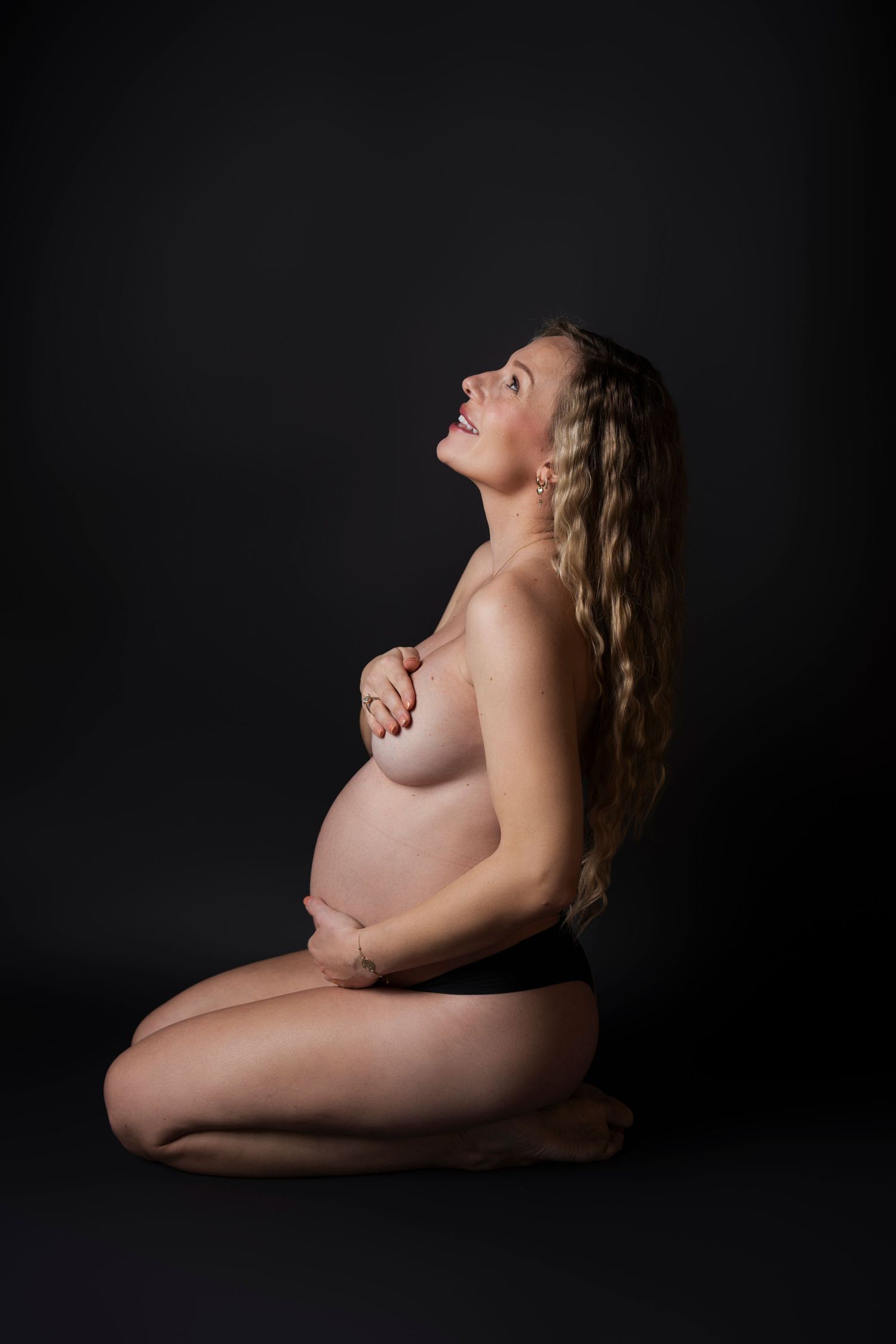 Side view maternity portrait with dramatic studio lighting in black and white.
