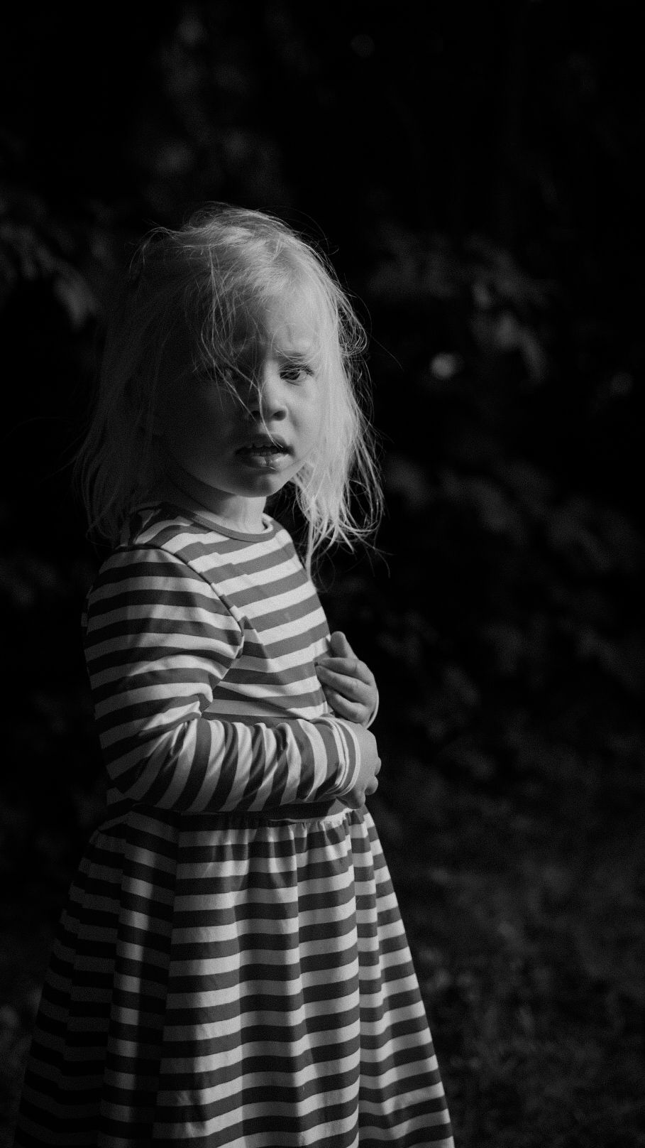 Black and white portrait of child wearing striped dress in dark setting.