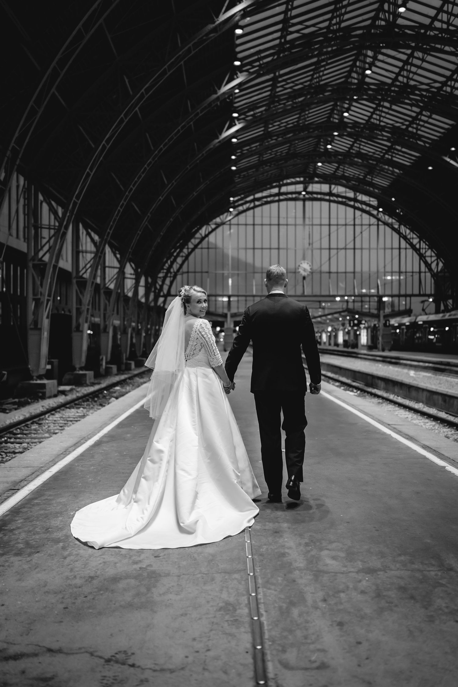 Brudepar går hånd i hånd på jernbanestasjon i Bergen - bryllupsfotografering By Karlstad