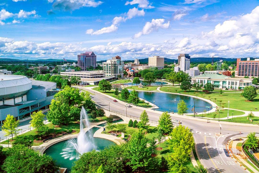 Aerial view of Huntsville, Alabama downtown skyline with fountain, green park, and pond on a sunny day.