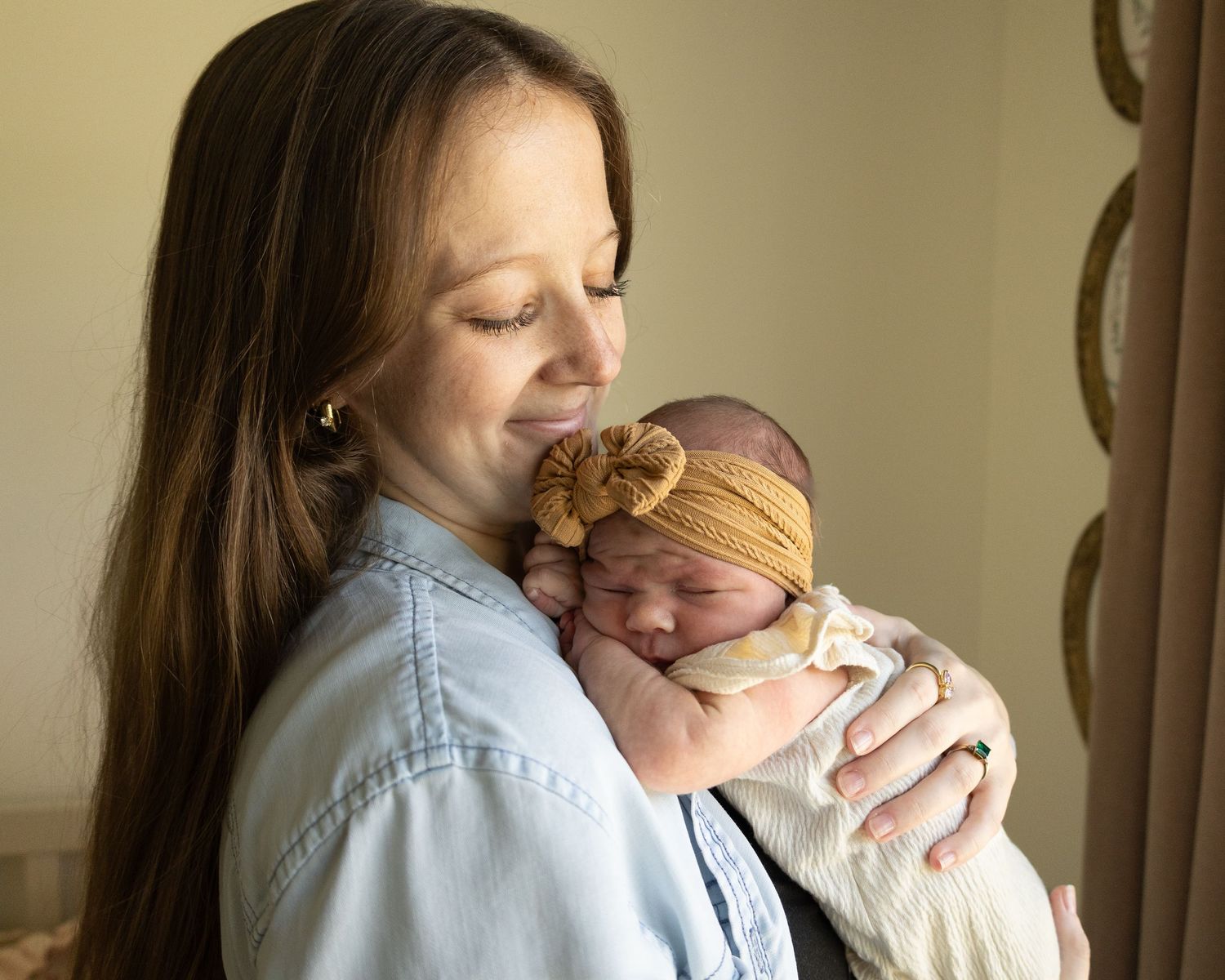Mother holding her newborn baby during an in-A young mother tenderly holds her sleeping newborn baby wearing a mustard yellow knit headband.