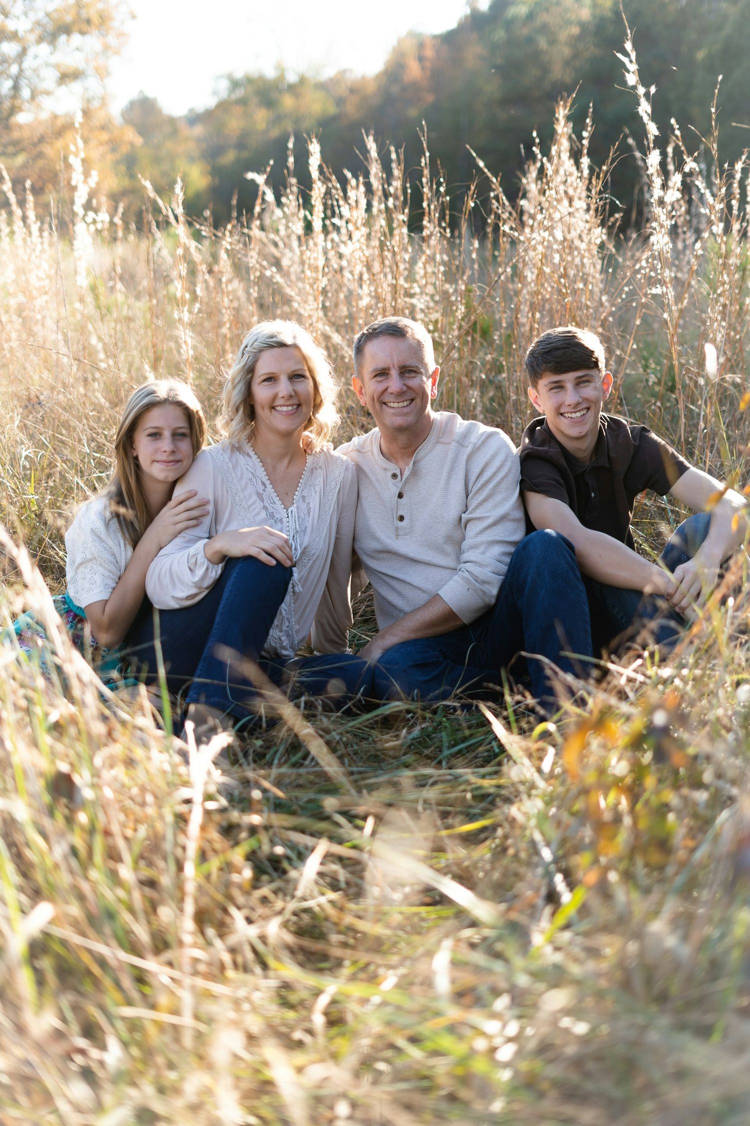 Family of four smiling together in a golden field of tall grass during autumn, enjoying an outdoor portrait session.