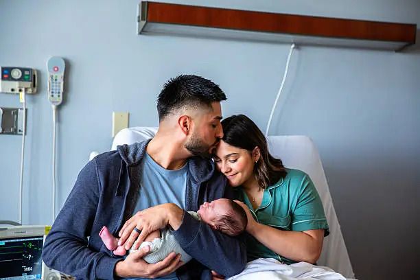 New parents share a tender moment with their newborn baby in a hospital room after delivery.