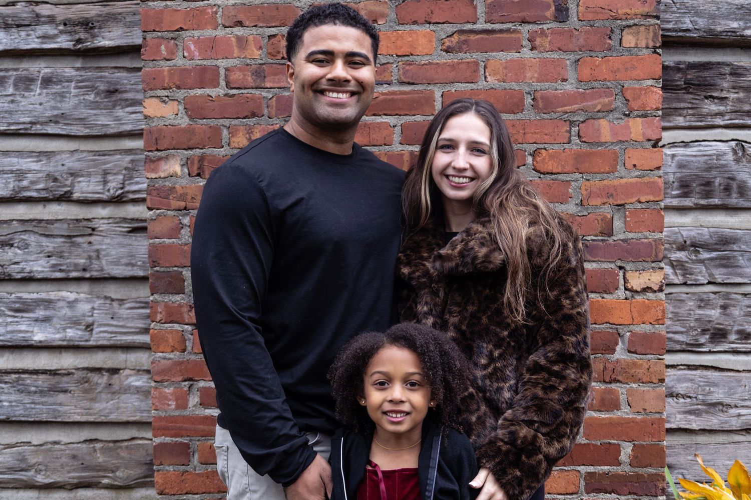 A family poses together against a rustic brick wall background.