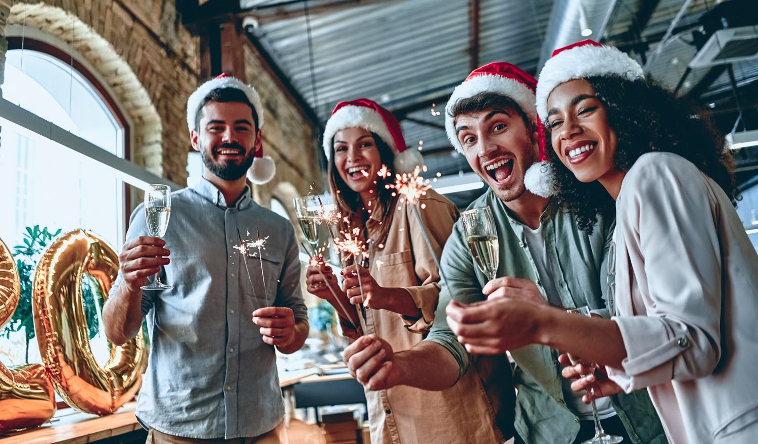 Company holiday party photography featuring four coworkers wearing Santa hats, holding sparklers, and celebrating together.