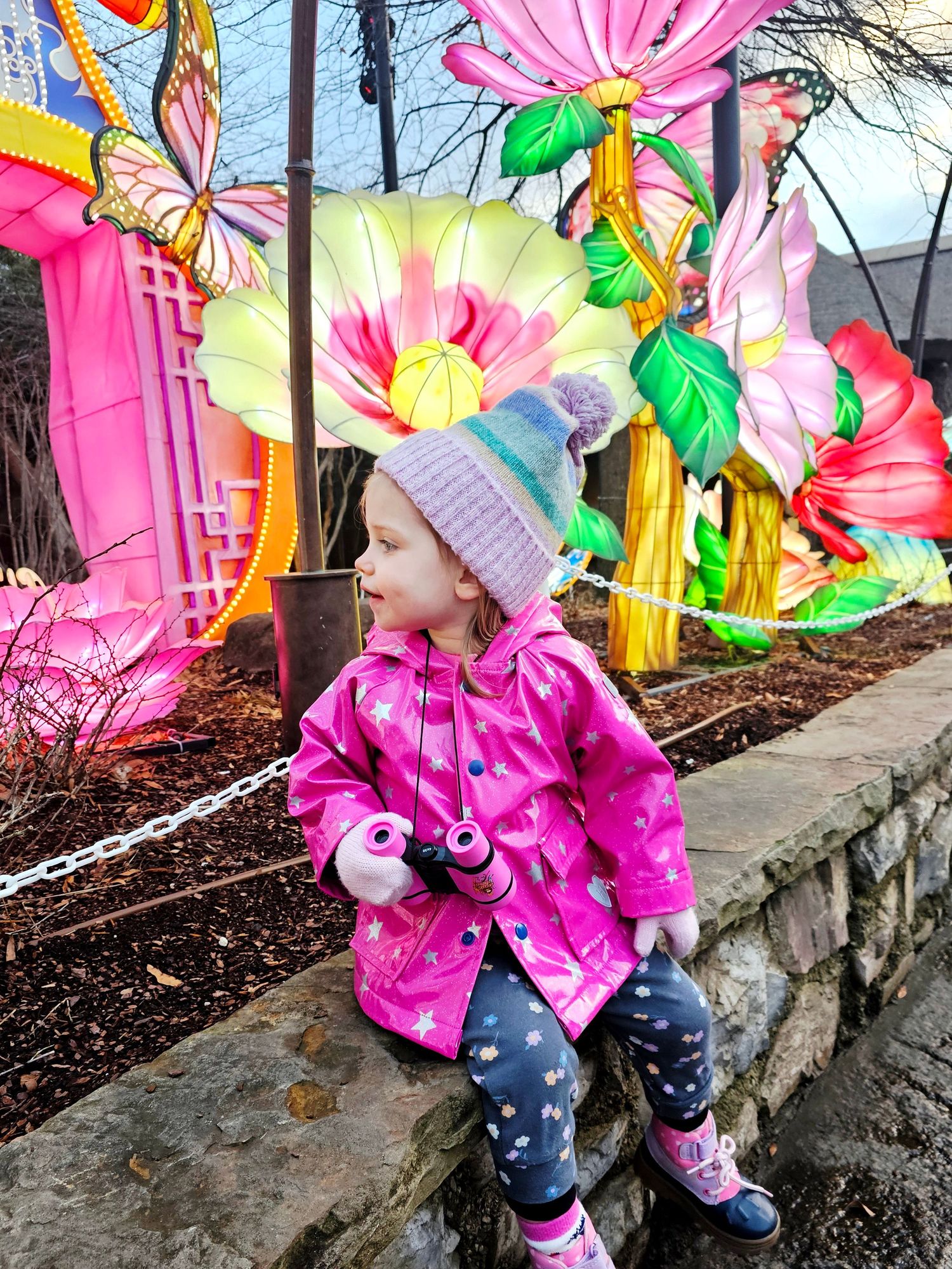 Child in pink jacket poses against colorful butterfly mural wall art.